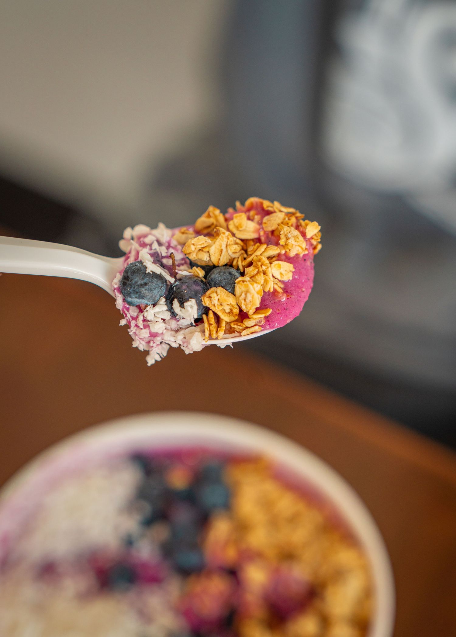 Blueberries and granola scattered on a wooden surface with a pink napkin and bowl in soft focus.