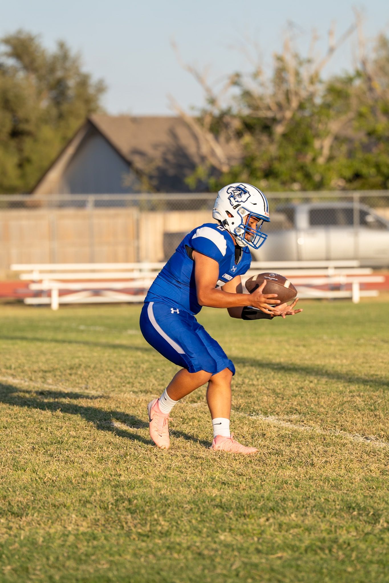 Football player in blue uniform crouches down on grassy field during practice drill.