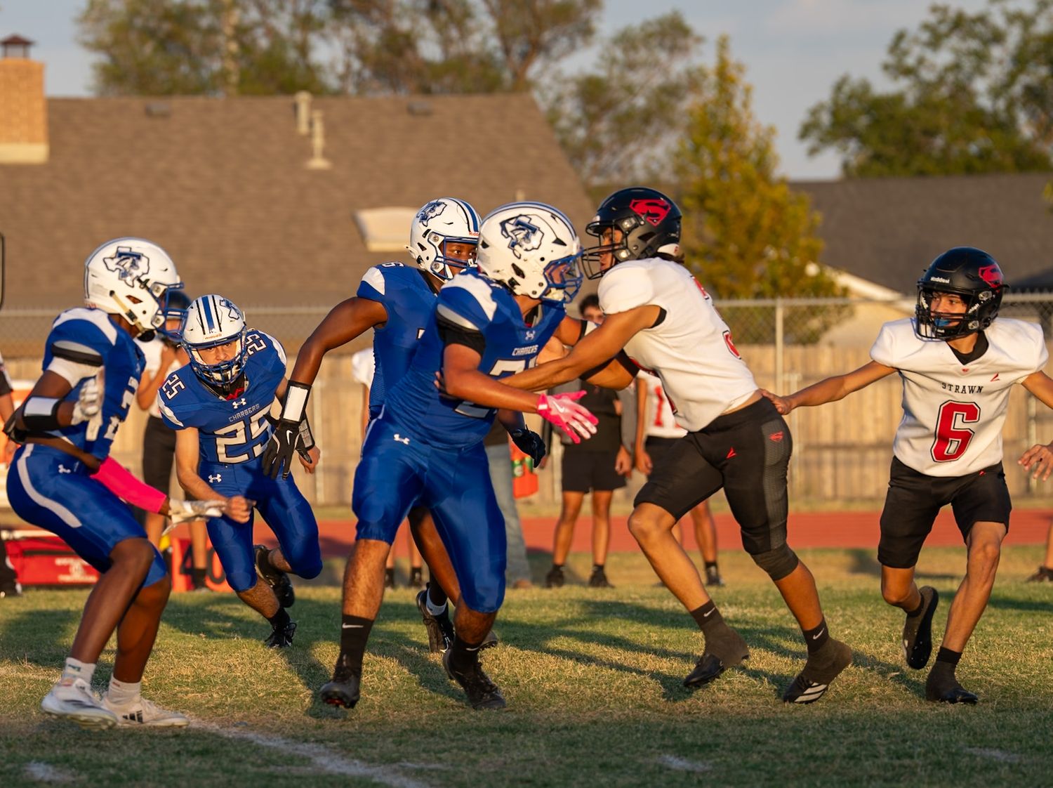 Football players line up at scrimmage during practice on a sunny afternoon.