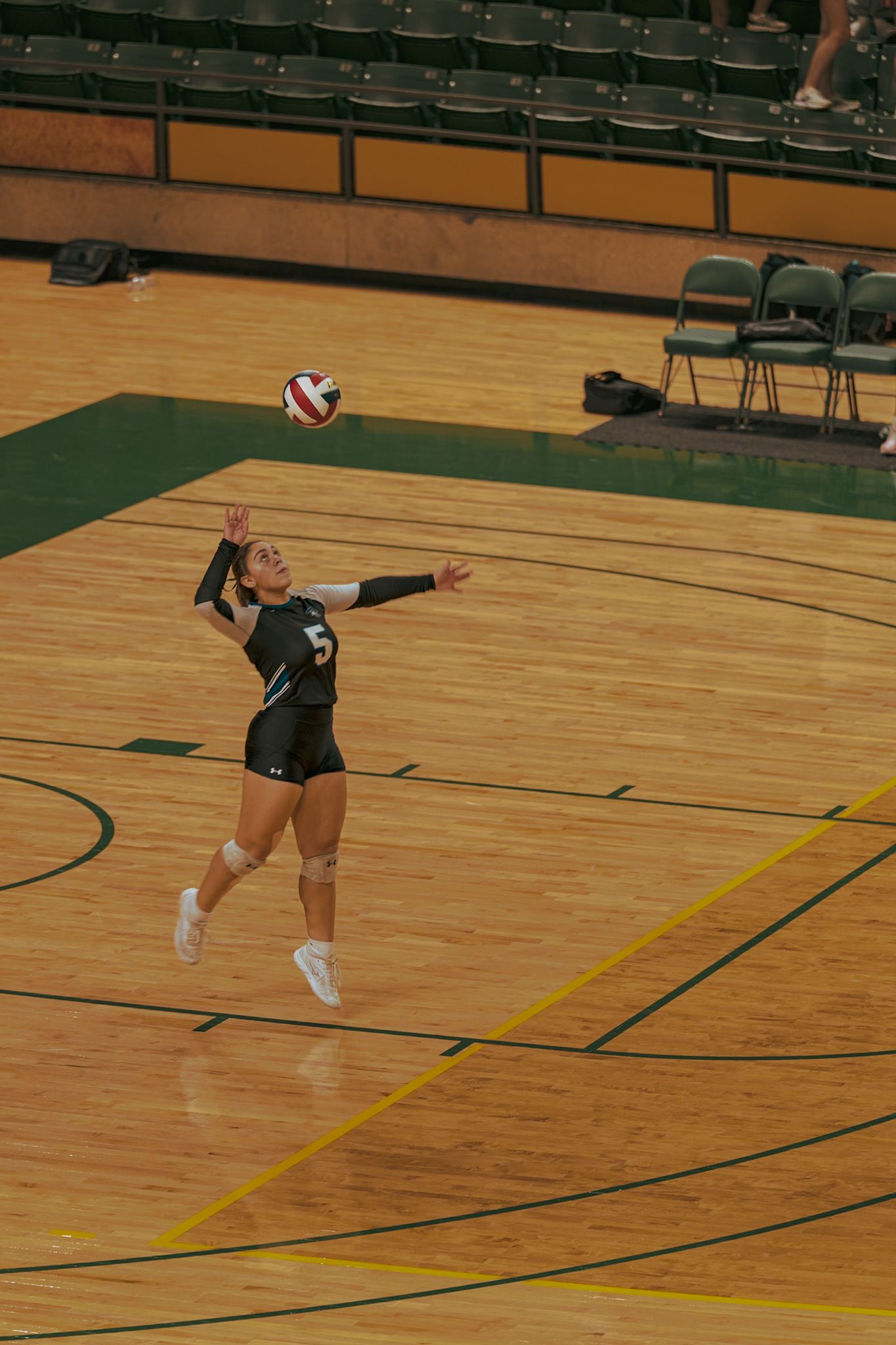 Volleyball player in dark uniform performs a diving save during indoor match on wooden court.