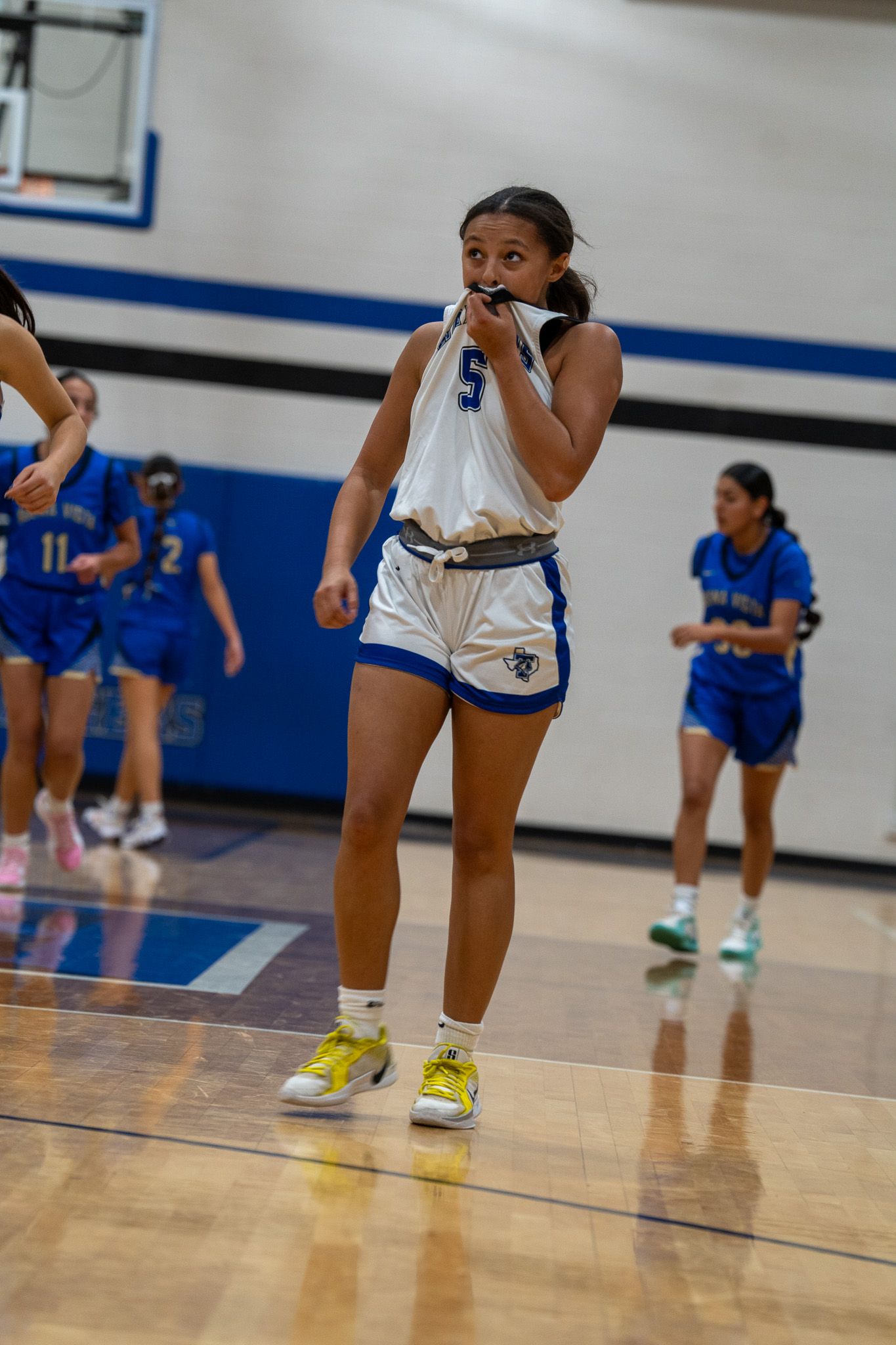 Basketball players in blue and white uniforms positioned low in defensive stance during game.