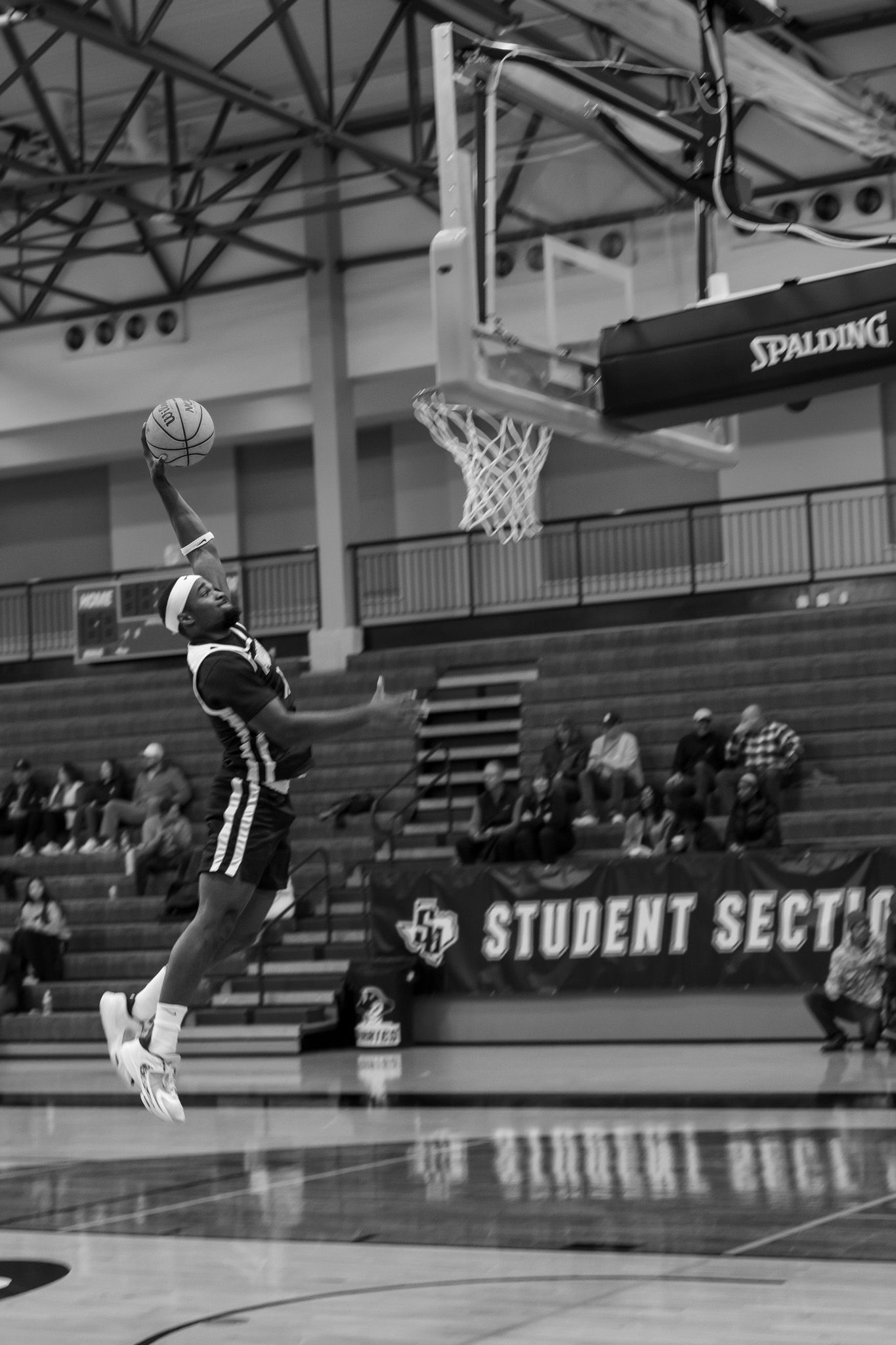 Black and white sequence photo of a basketball player performing a slam dunk in an indoor gymnasium.