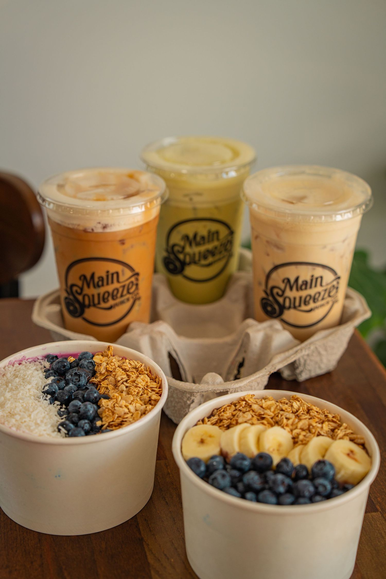 Fresh acai bowls topped with blueberries, sliced bananas, and granola served alongside smoothie drinks in branded cups.