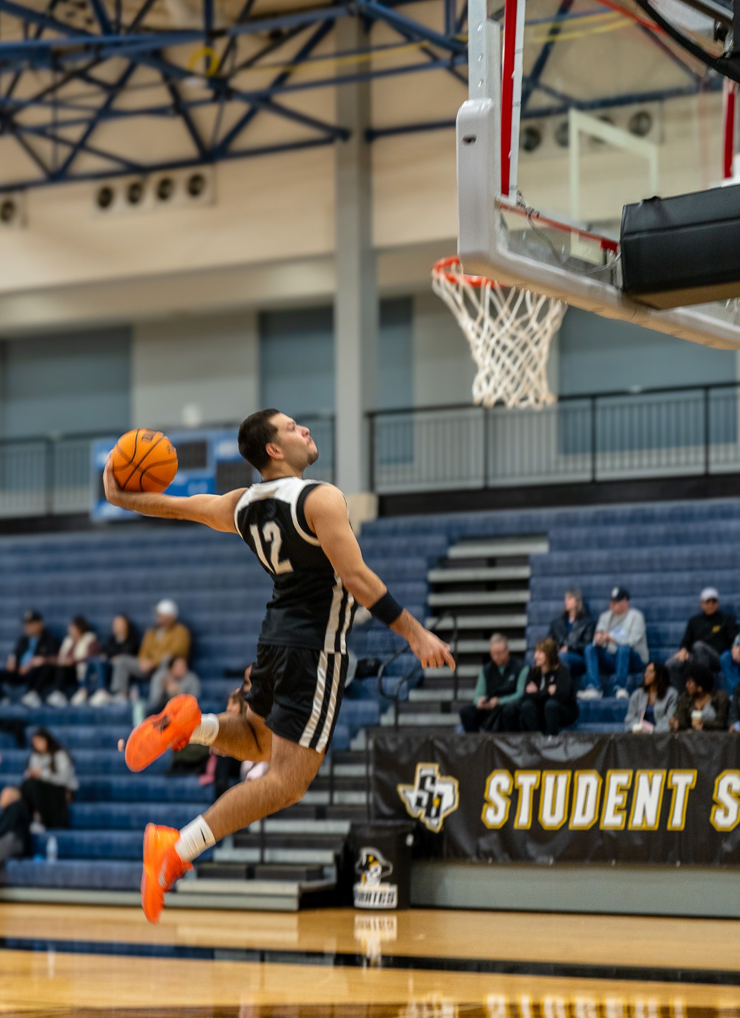 Basketball player leaps high for a slam dunk attempt in a gymnasium during a competitive game.