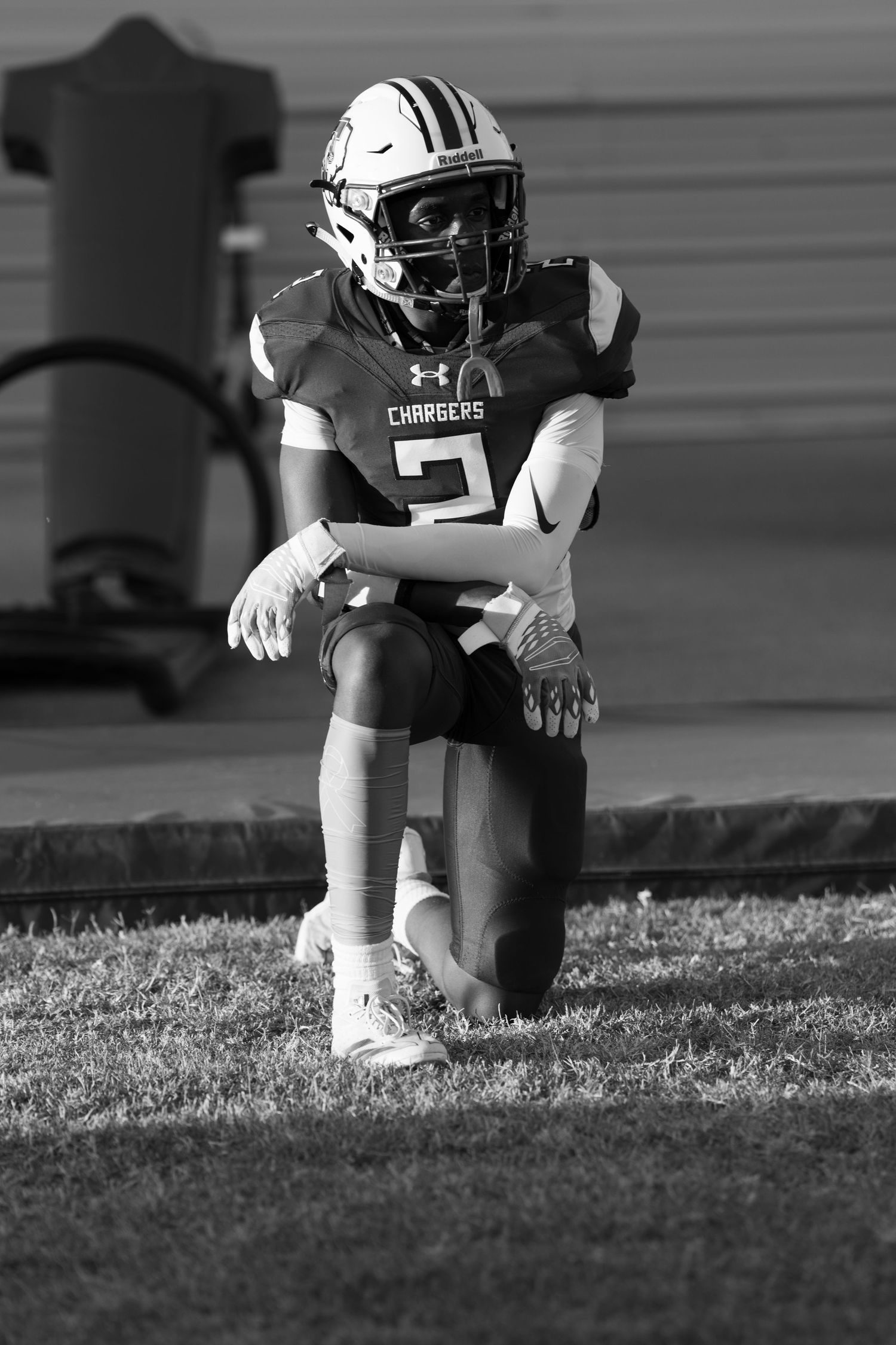 Black and white photo of a football player in Under Armour uniform kneeling on field during practice.