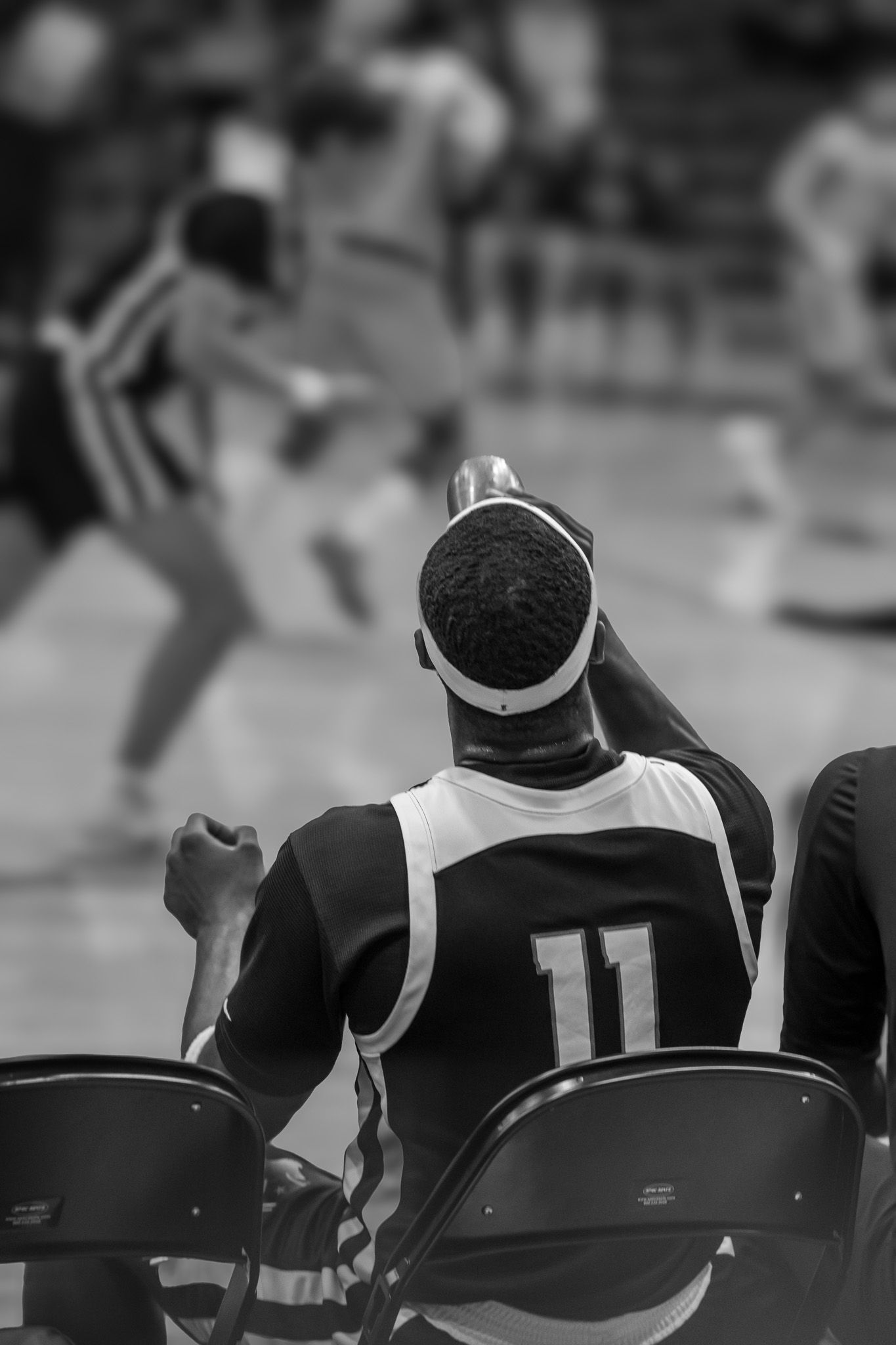 Black and white photo showing basketball players sitting on sideline chairs during a game.