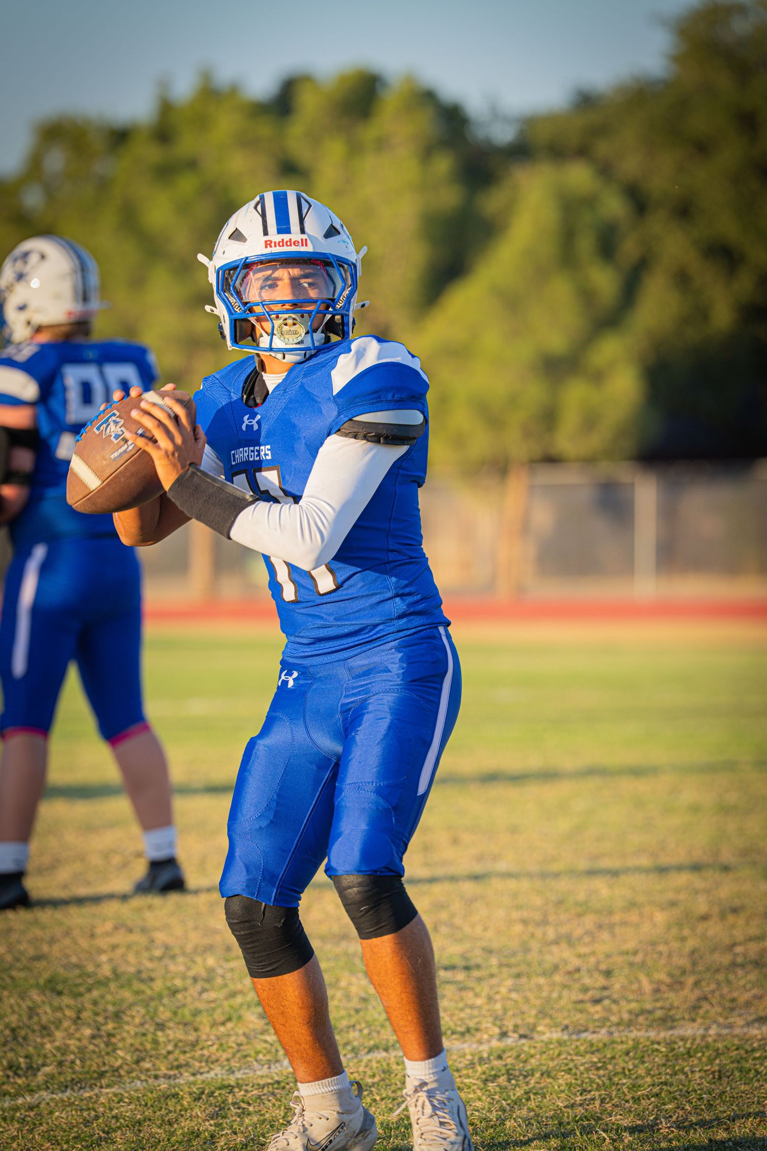 Football players in blue uniforms practice drills on a sunny field during training session.