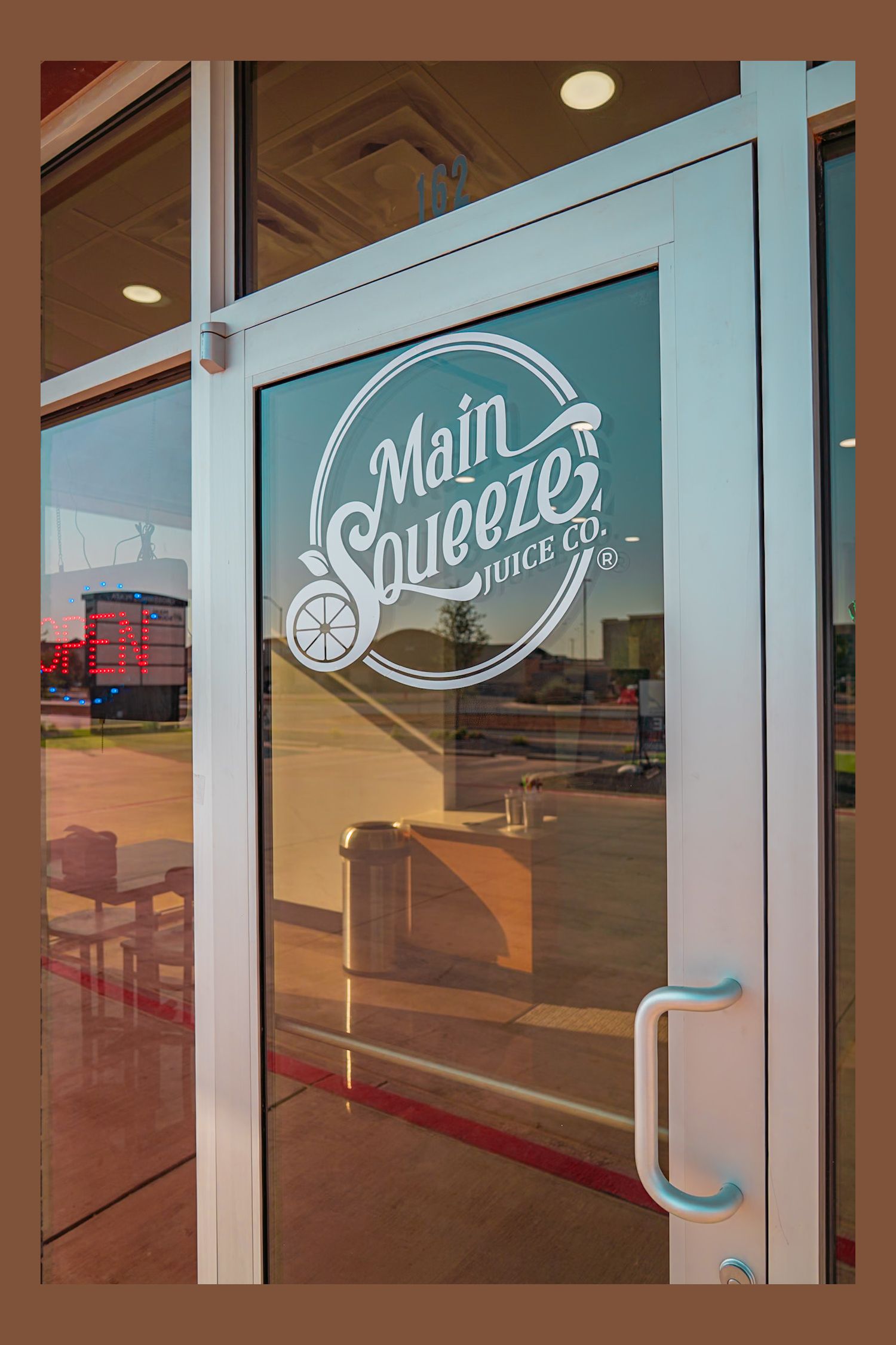 Glass door with turquoise 'Main Squeezes Juice Bar' logo and circular citrus fruit design decal.