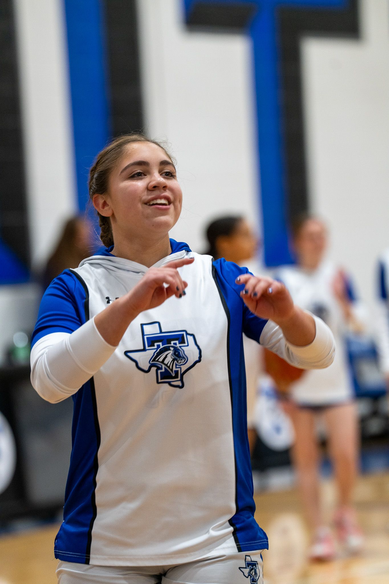 A volleyball player in a white and blue uniform sets the ball during an indoor match.