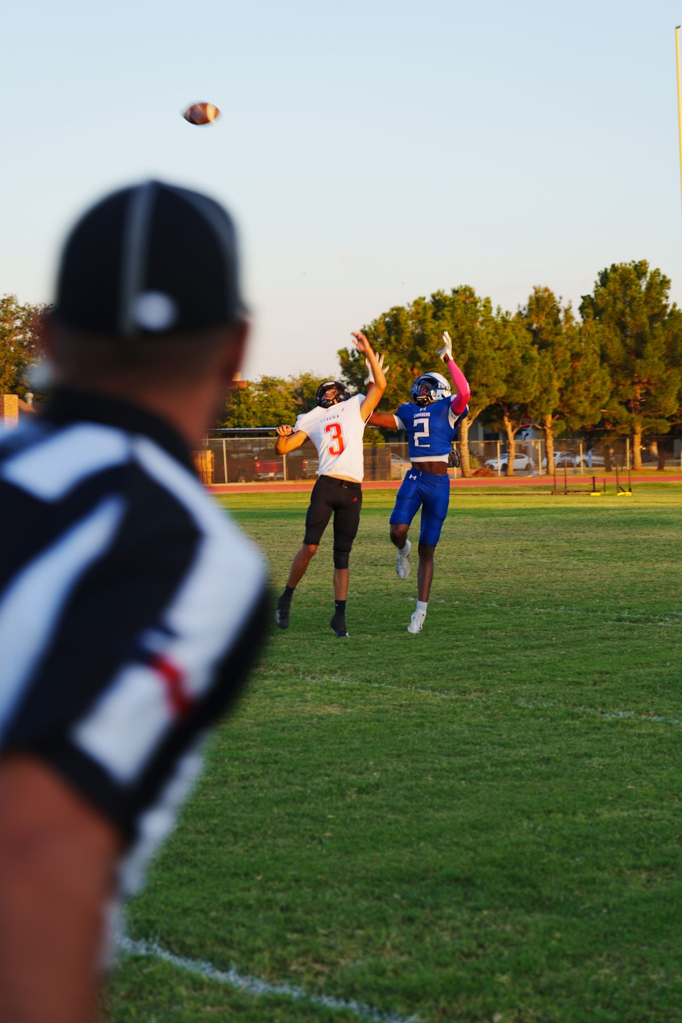 Football soars through the air on sunny field with players in background during practice.