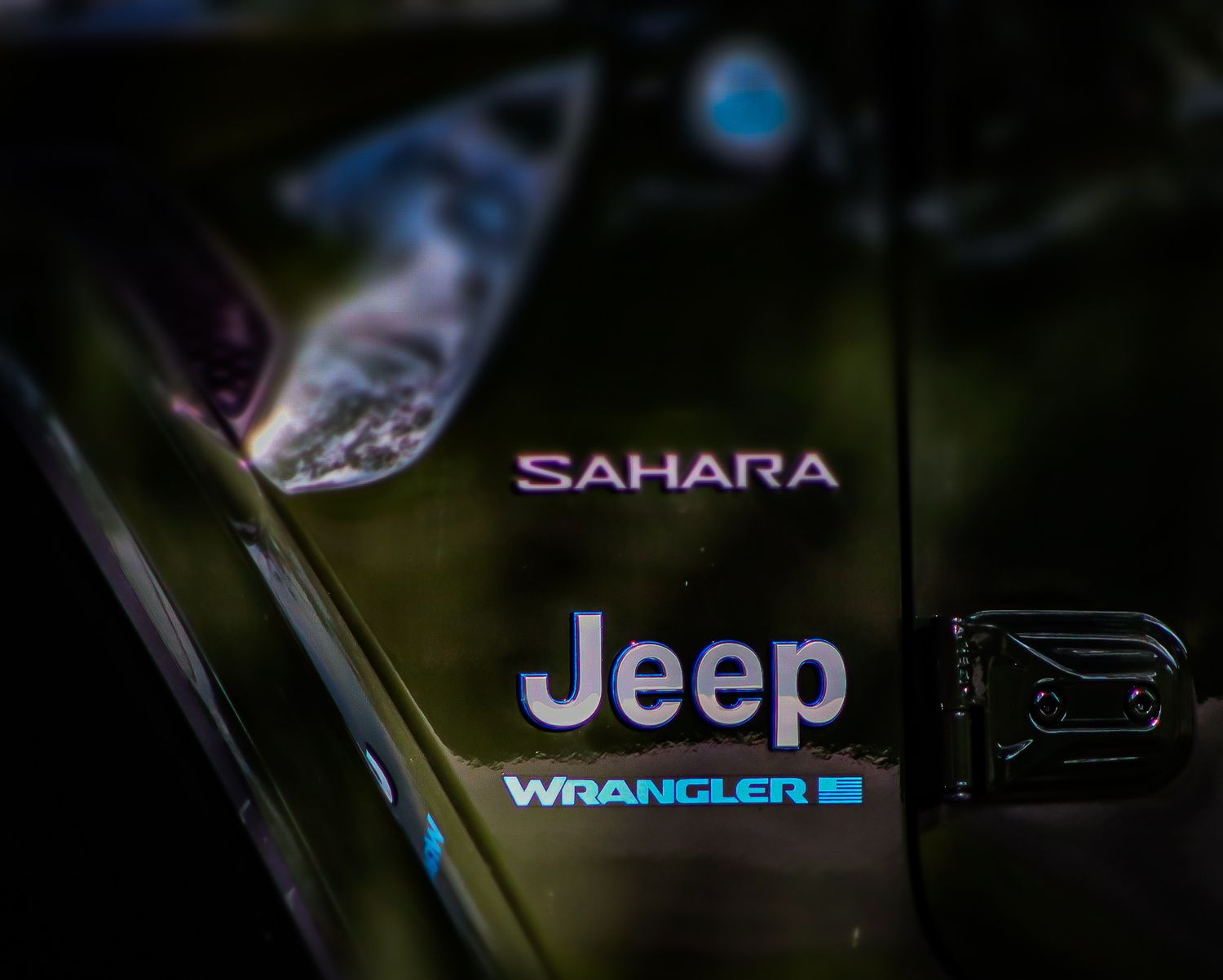 Close-up of Jeep Wrangler Sahara badging on dark vehicle exterior.