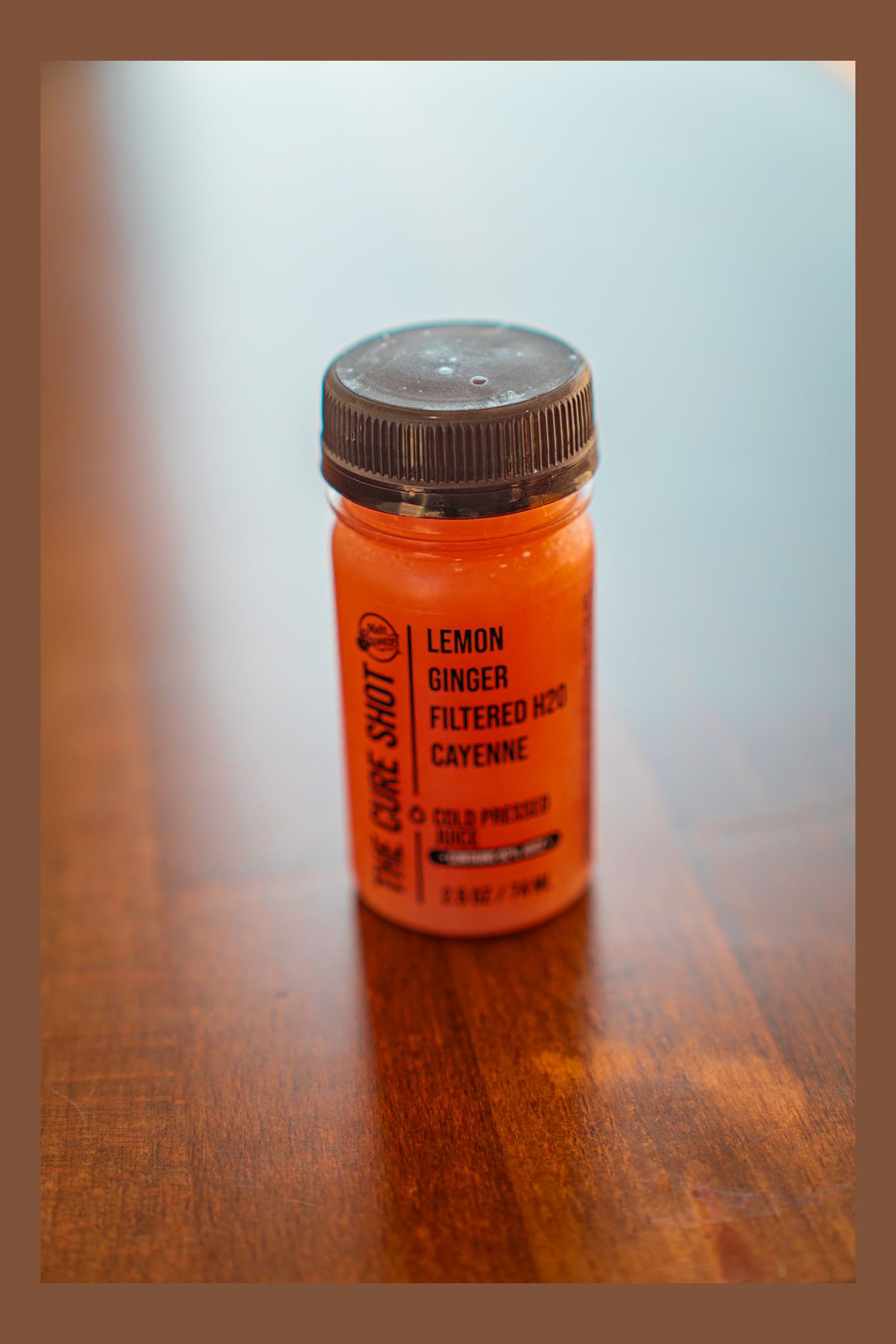 An orange bottle of lemon ginger cayenne wellness shot sits on a wooden surface in soft lighting.