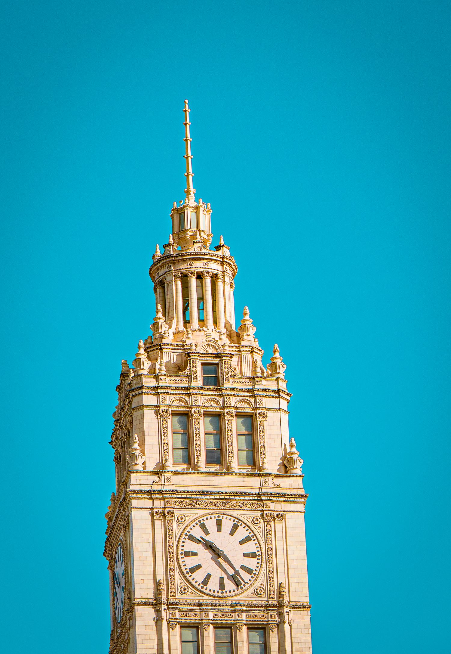 Ornate clock tower with golden architectural details against vibrant turquoise sky in Chicago's Wrigley Building.