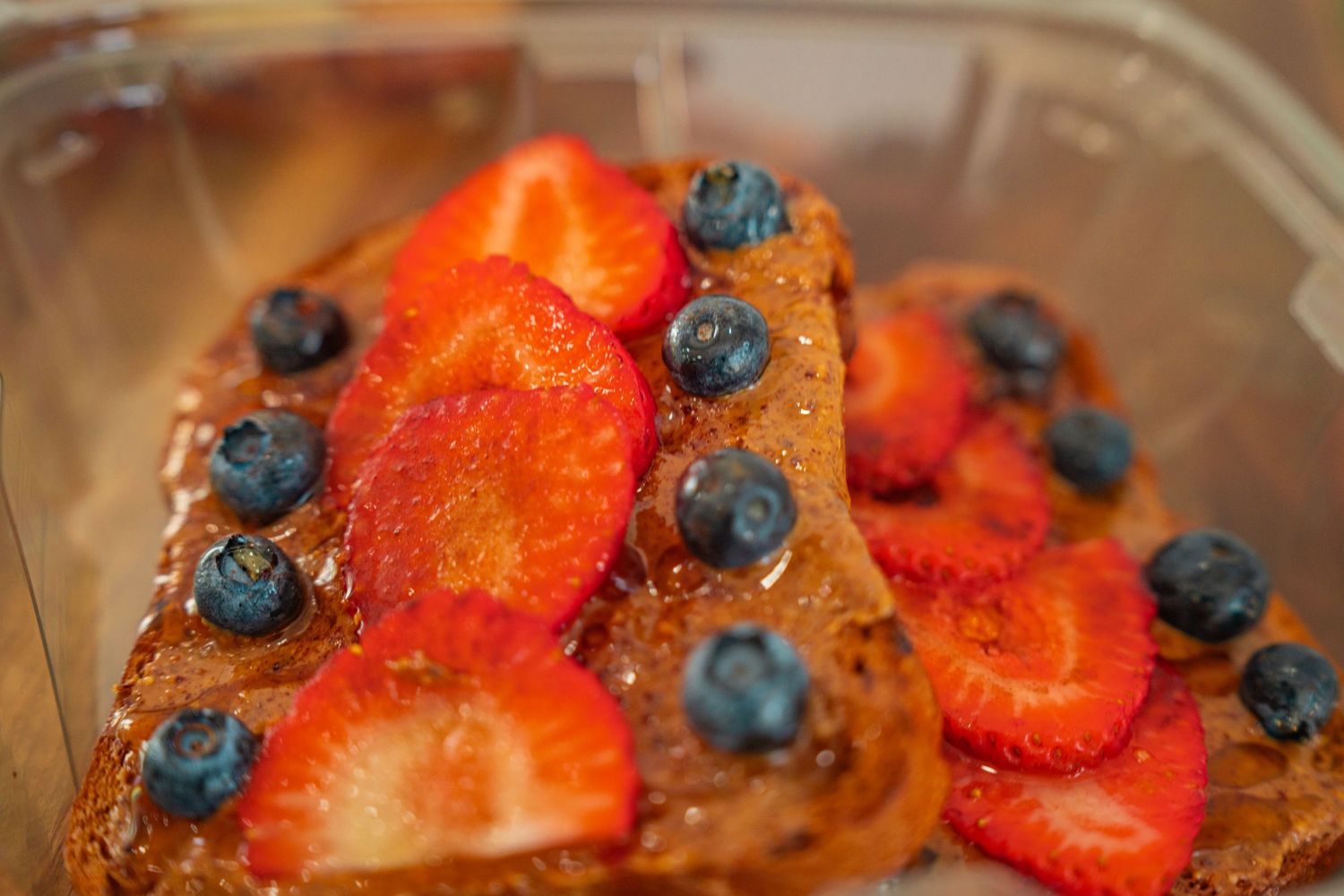 Fresh waffles topped with vibrant strawberries and blueberries drizzled with syrup on a wooden surface.