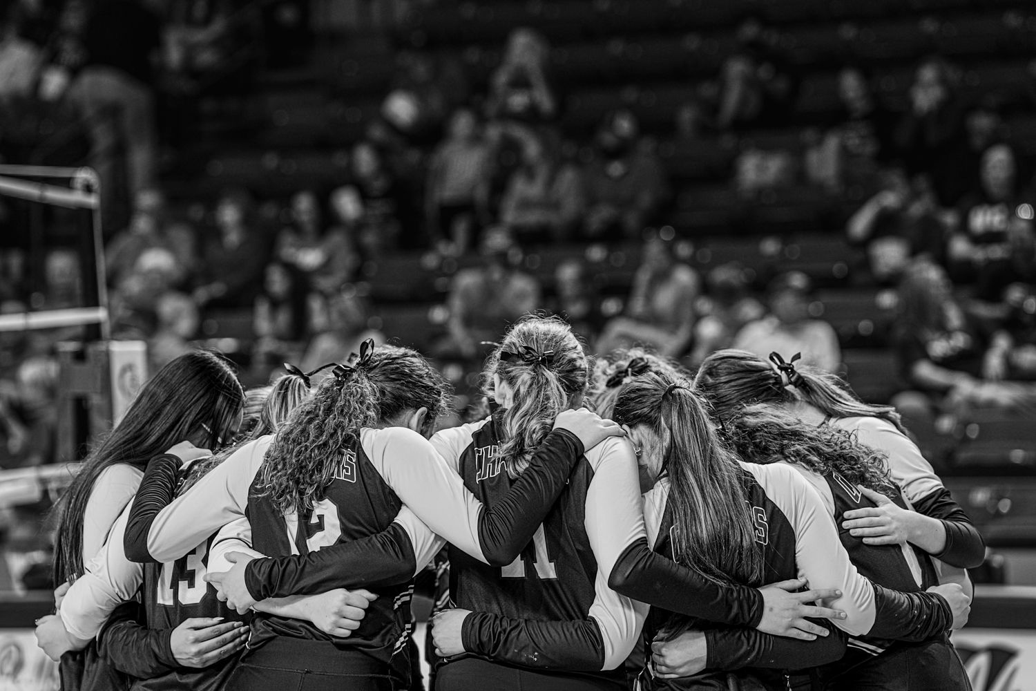 Team members huddle together with arms around each other in solidarity on a basketball court.