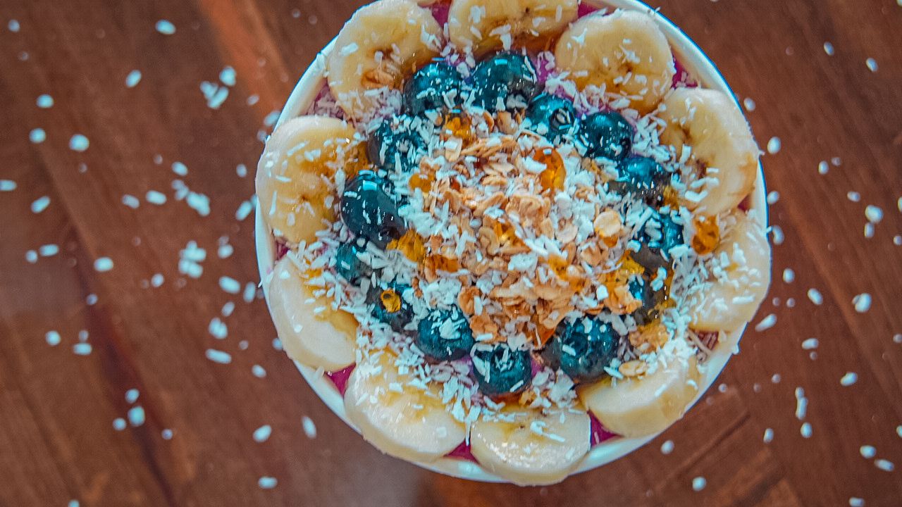 Colorful smoothie bowl topped with blue spirulina, bananas, coconut flakes and orange powder on wooden surface.