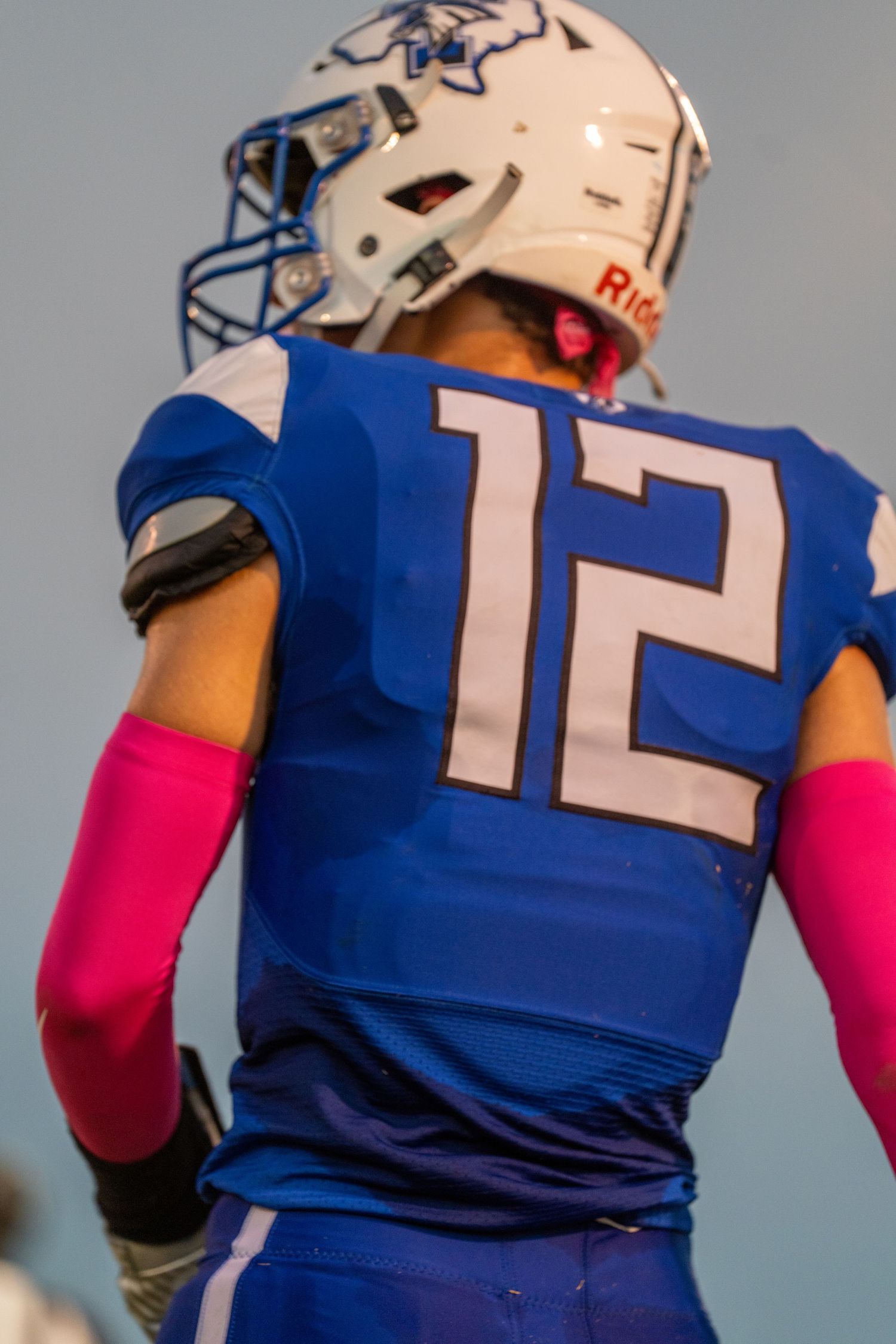 Football player wearing blue jersey with number 12 and bright pink arm sleeves on the field during a game.