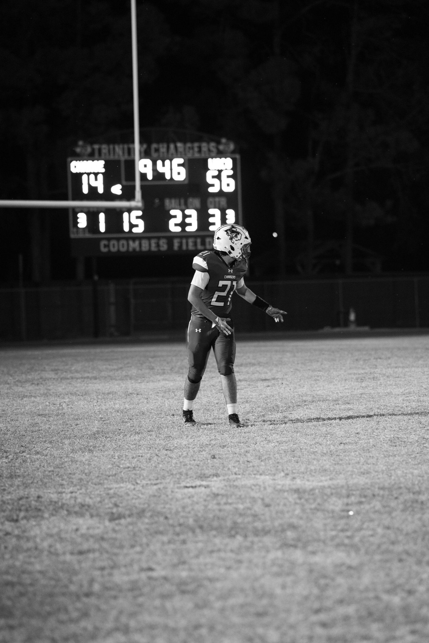 Football player stands on field at night with illuminated scoreboard visible in background.