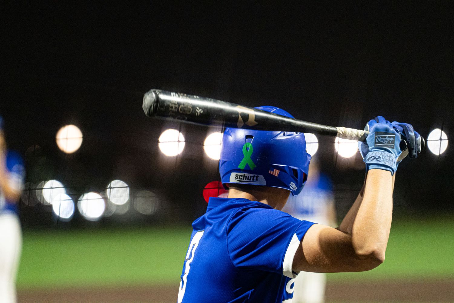 Baseball player in blue uniform swings bat during nighttime game with stadium lights illuminating the field.