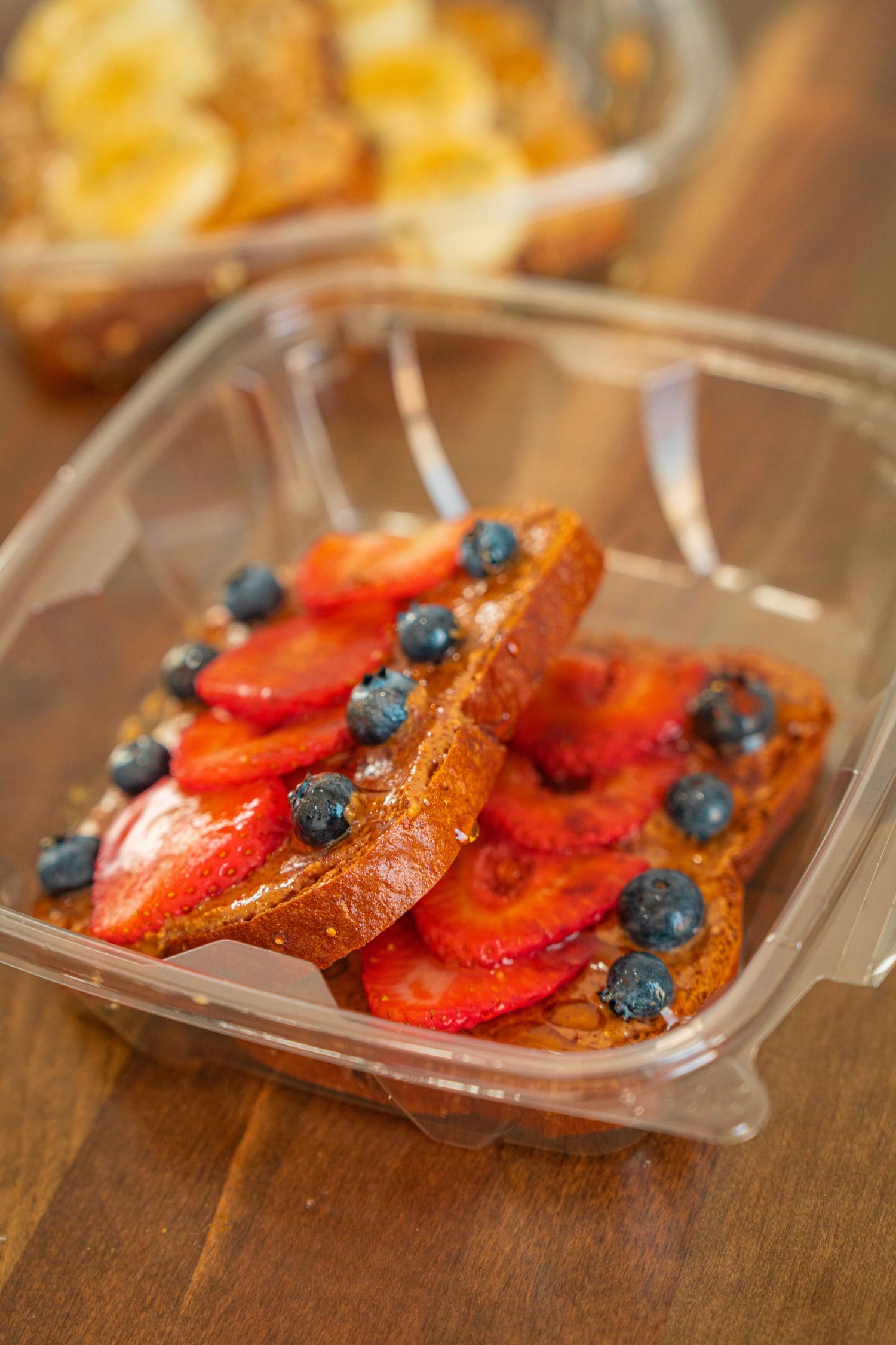French toast topped with fresh strawberries and blueberries served on a clear plastic plate on wooden surface.