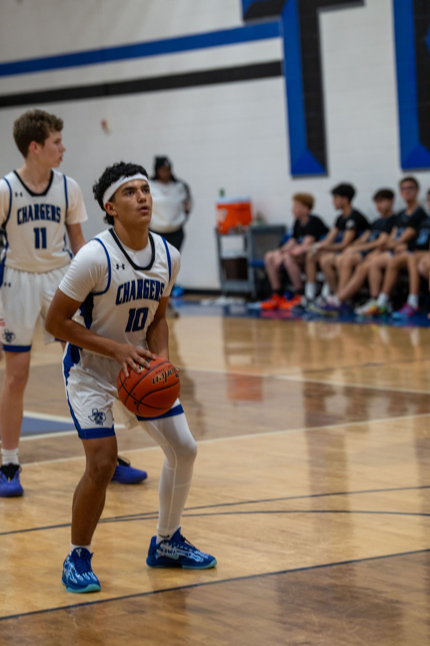 Basketball players in blue and white uniforms kneel on the hardwood court during a game break.