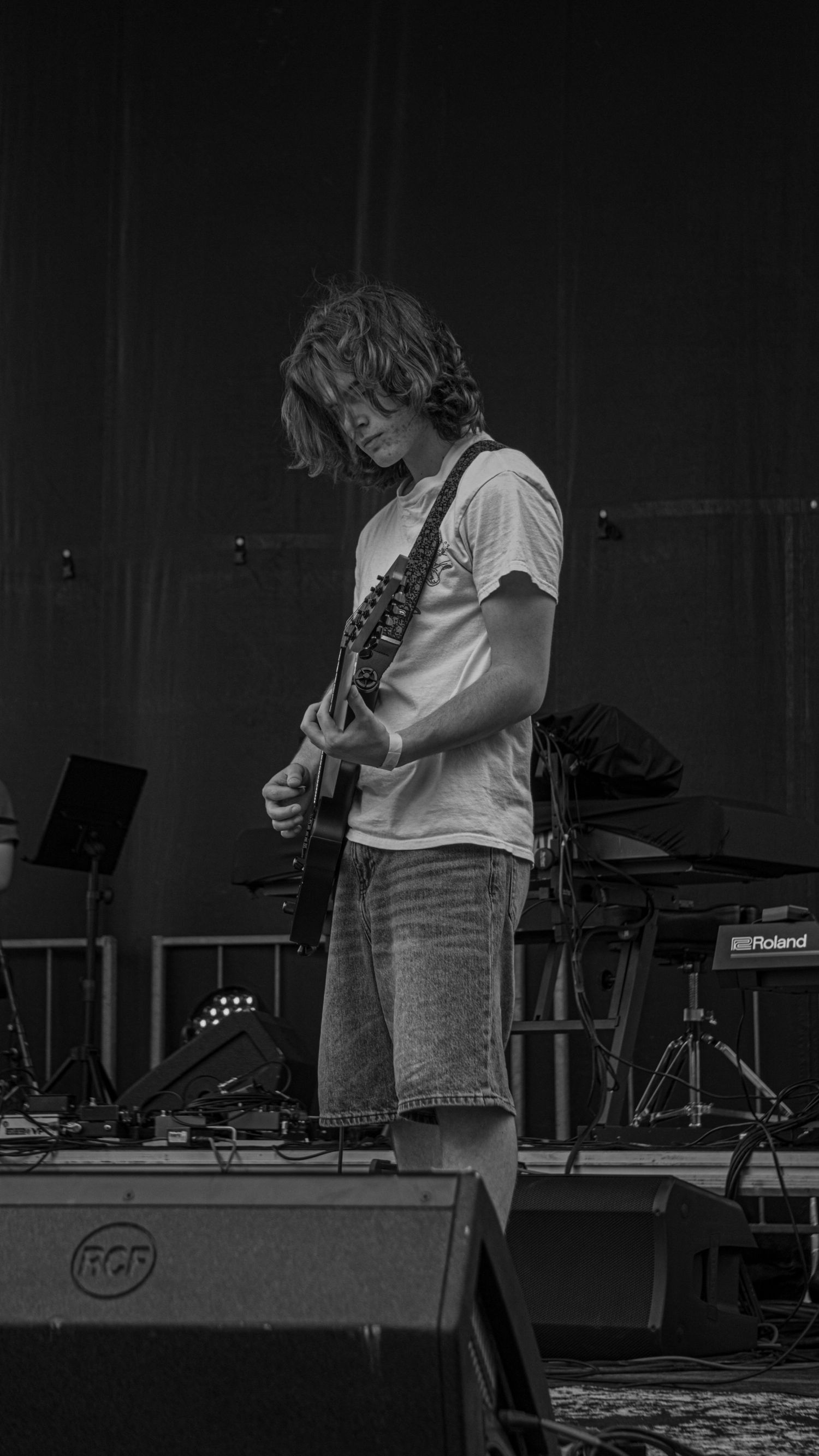 Black and white photo of a guitarist performing on stage with musical equipment visible in the background.