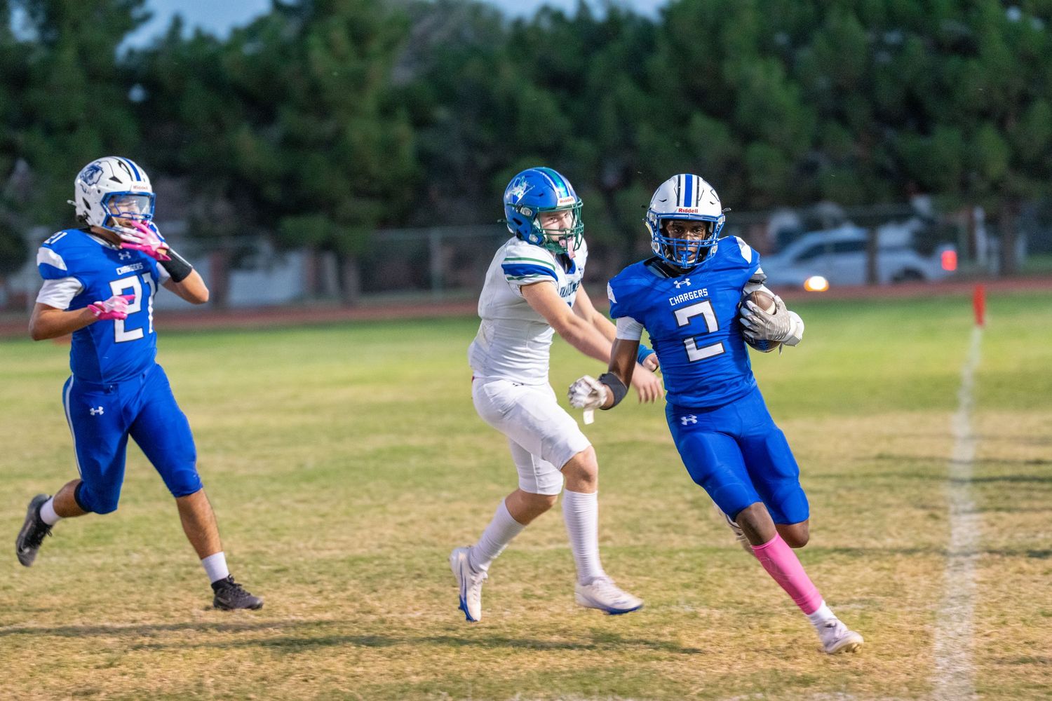 Football players collide during a tackle attempt on a grass field during a game in blue and white uniforms.