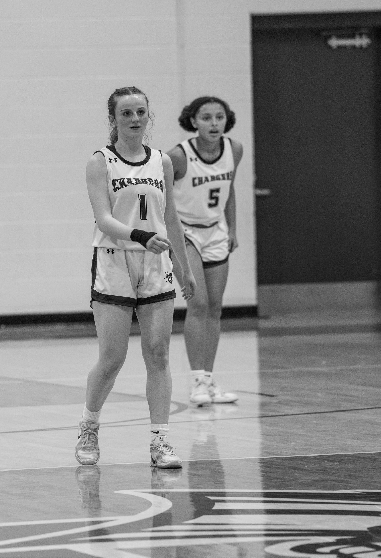 Basketball players crouch in defensive stance positions on a gymnasium court during practice.