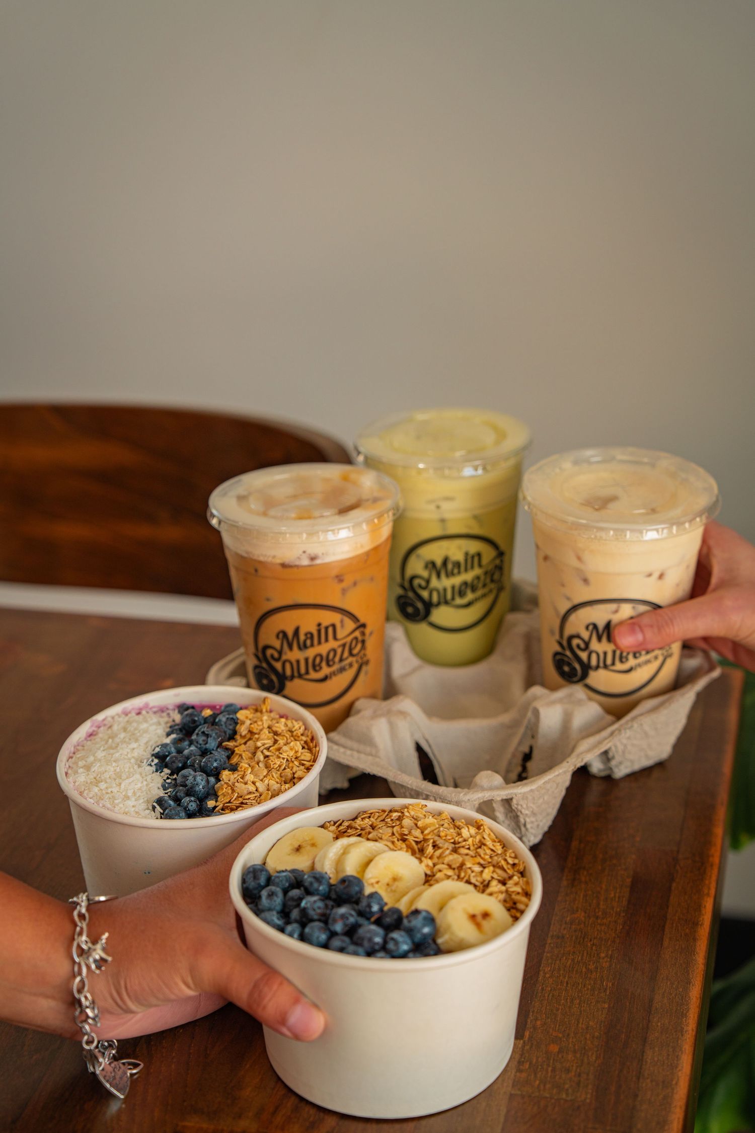 A healthy breakfast bowl with blueberries, granola and smoothies arranged in a progression sequence on a wooden table.
