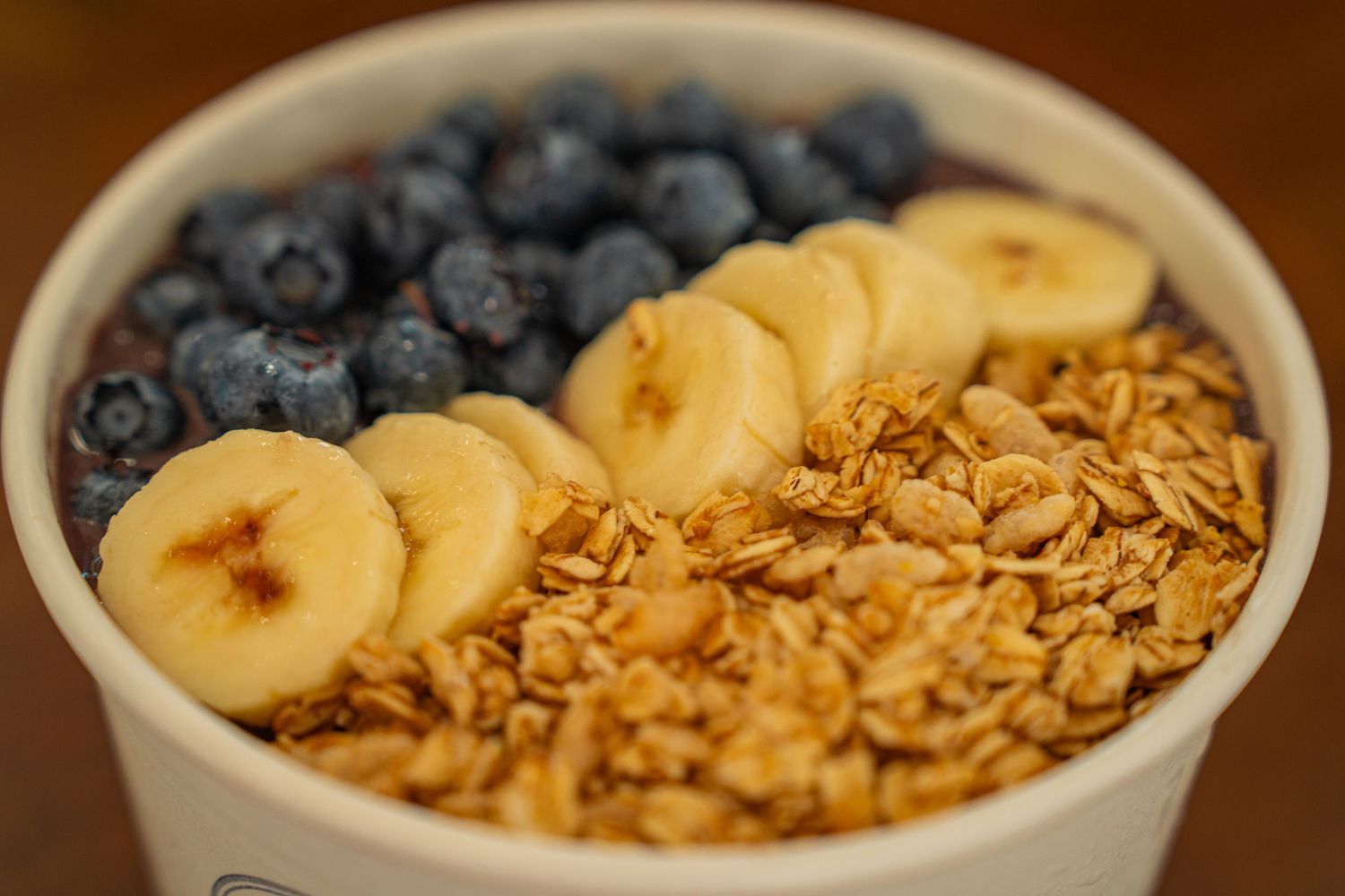 Fresh blueberries, sliced bananas, and crunchy granola are layered in a white ceramic bowl for a healthy breakfast.