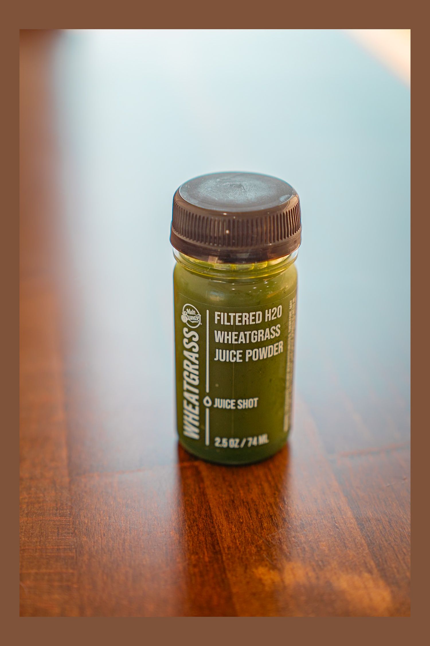 A glass jar of wheatgrass juice powder supplement photographed in sequence at different angles on a wooden table in natural light.