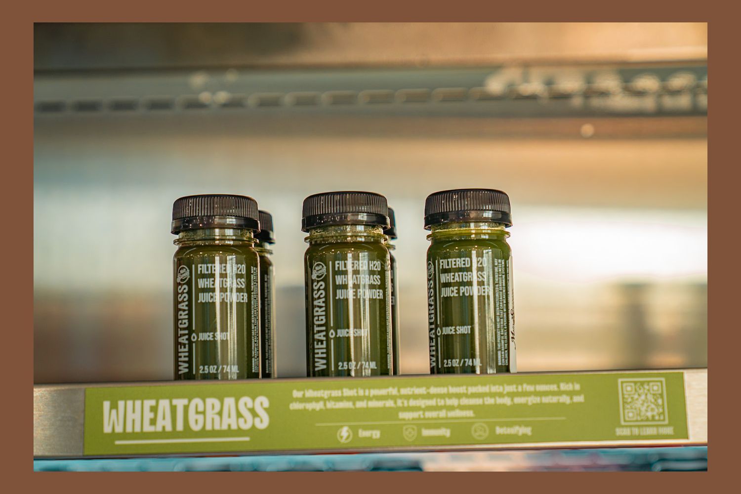 Three glass bottles of wheatgrass juice lined up on a shelf with a product label displayed underneath.