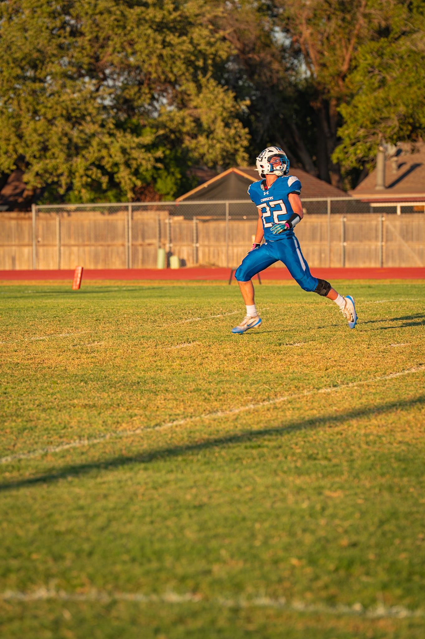 Soccer player in blue jersey slides across grass field during golden hour sunlight.