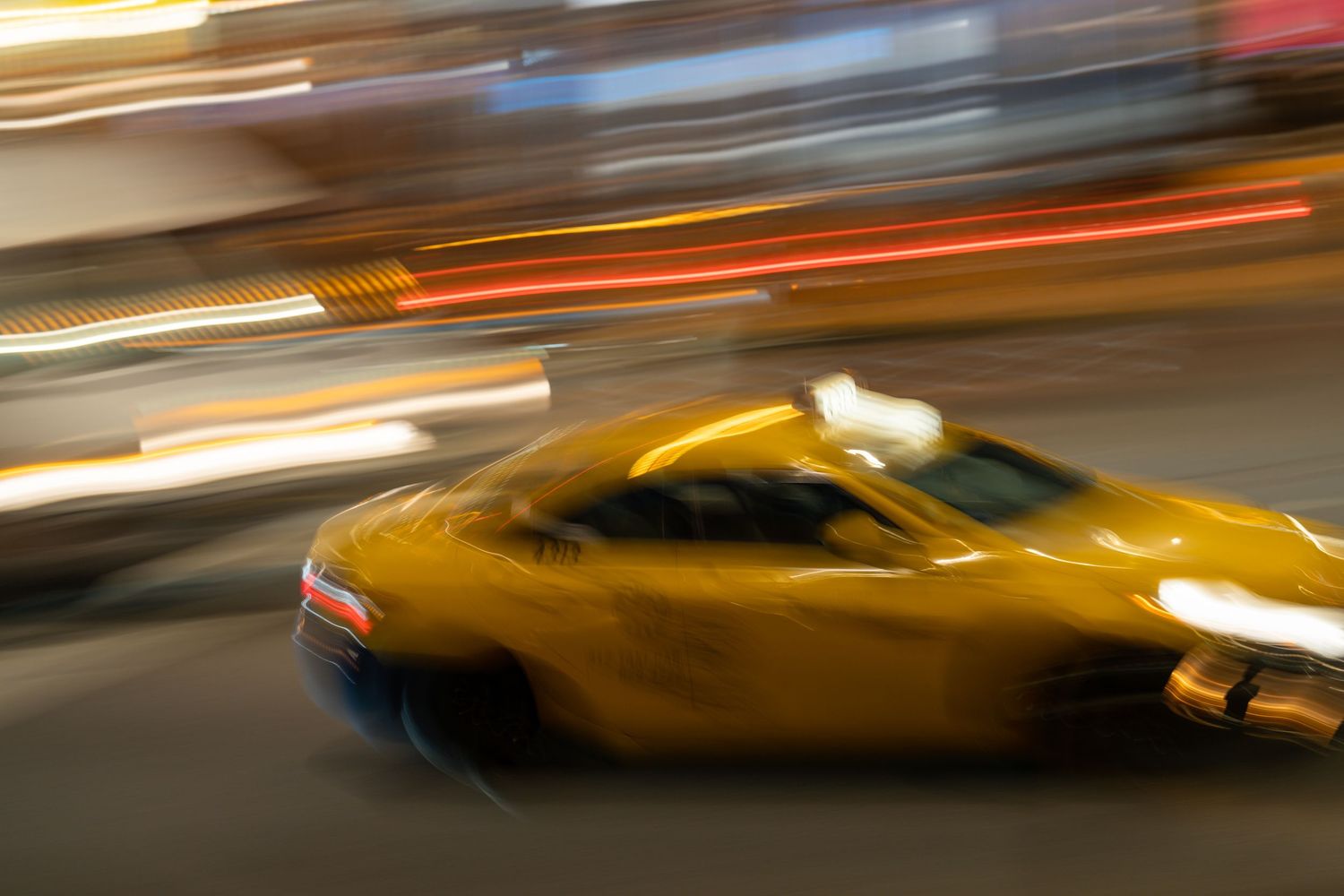 Motion blur of yellow taxi cab driving through city streets at night with streaks of light trails.