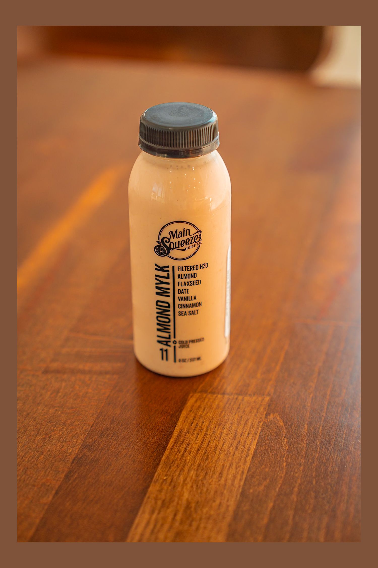 Eight small glass jars with black lids sit in a row on a wooden surface in ambient lighting.