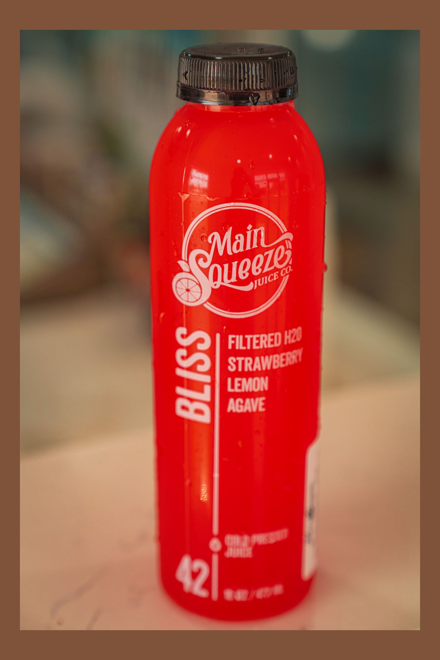 A bright red bottle of Melt Squeeze filtered acai strawberry lemon juice drink with a black cap against a blurred background.