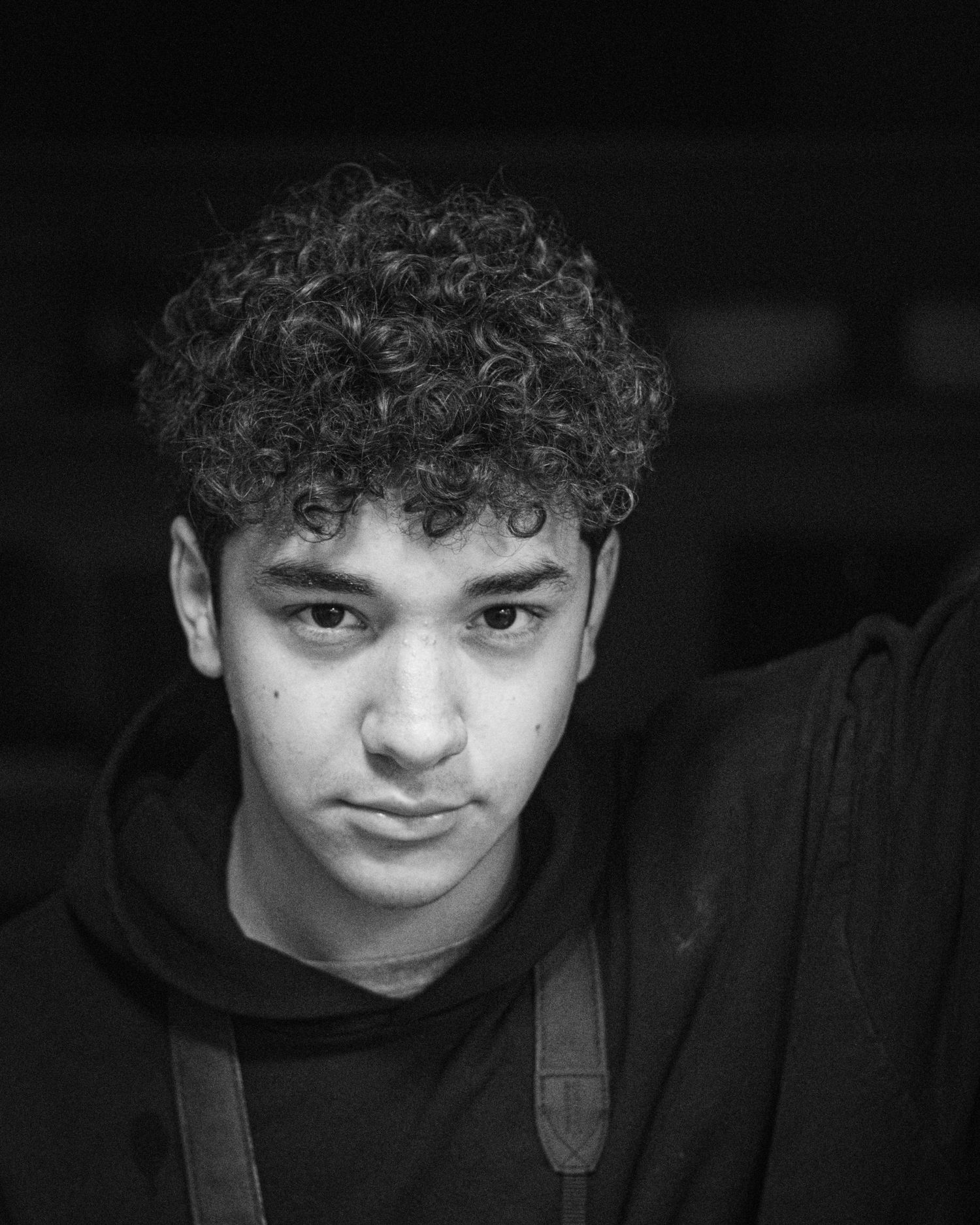 Portrait of a young person with curly hair wearing a black hoodie.