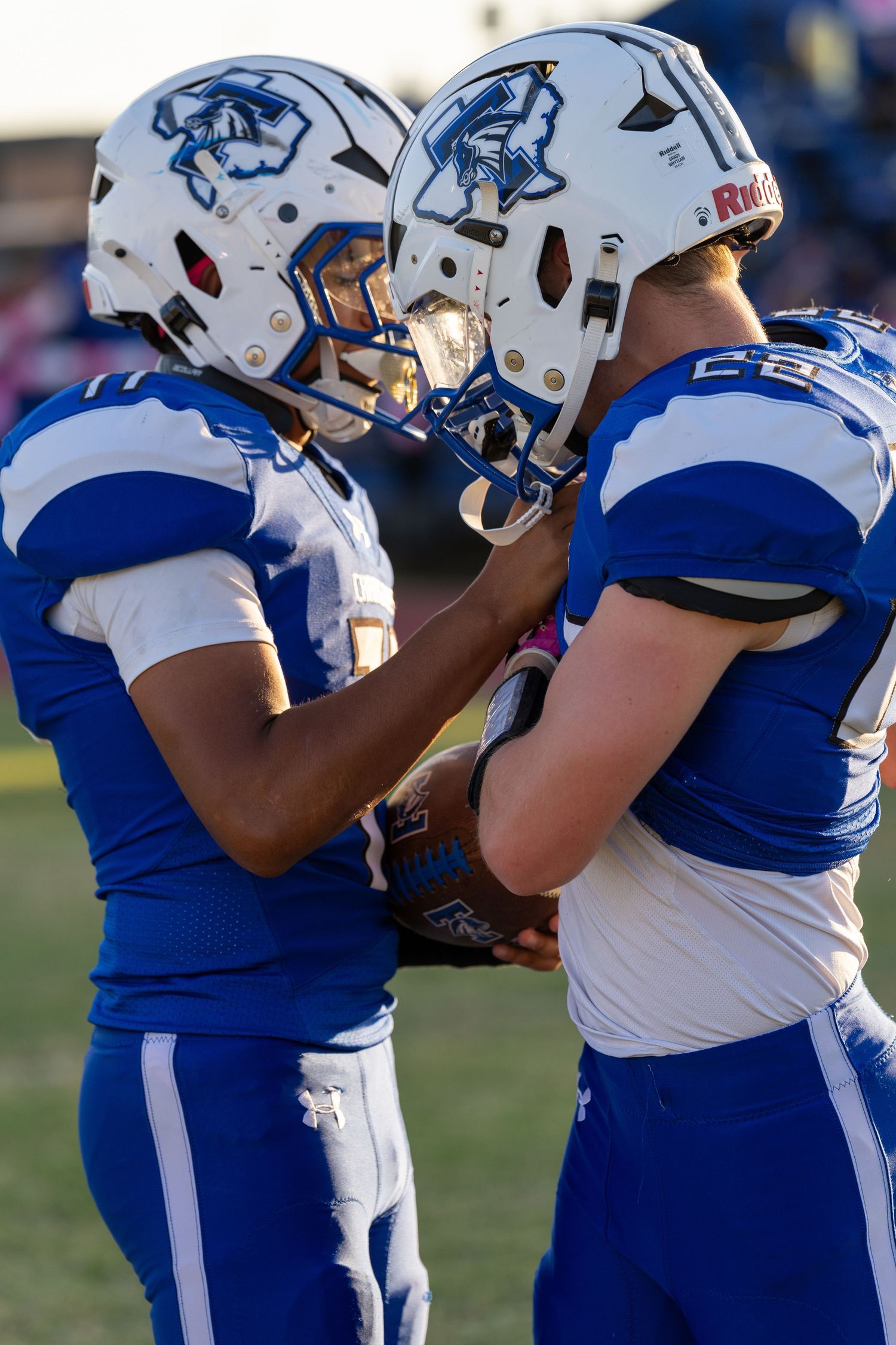 Football players in blue and white uniforms huddle together on the field during a game.