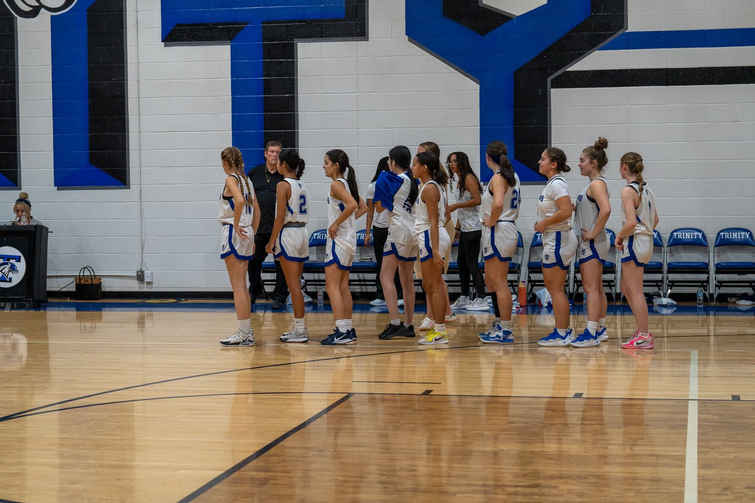 Basketball team huddles near the sideline during a game in a blue and white gymnasium.