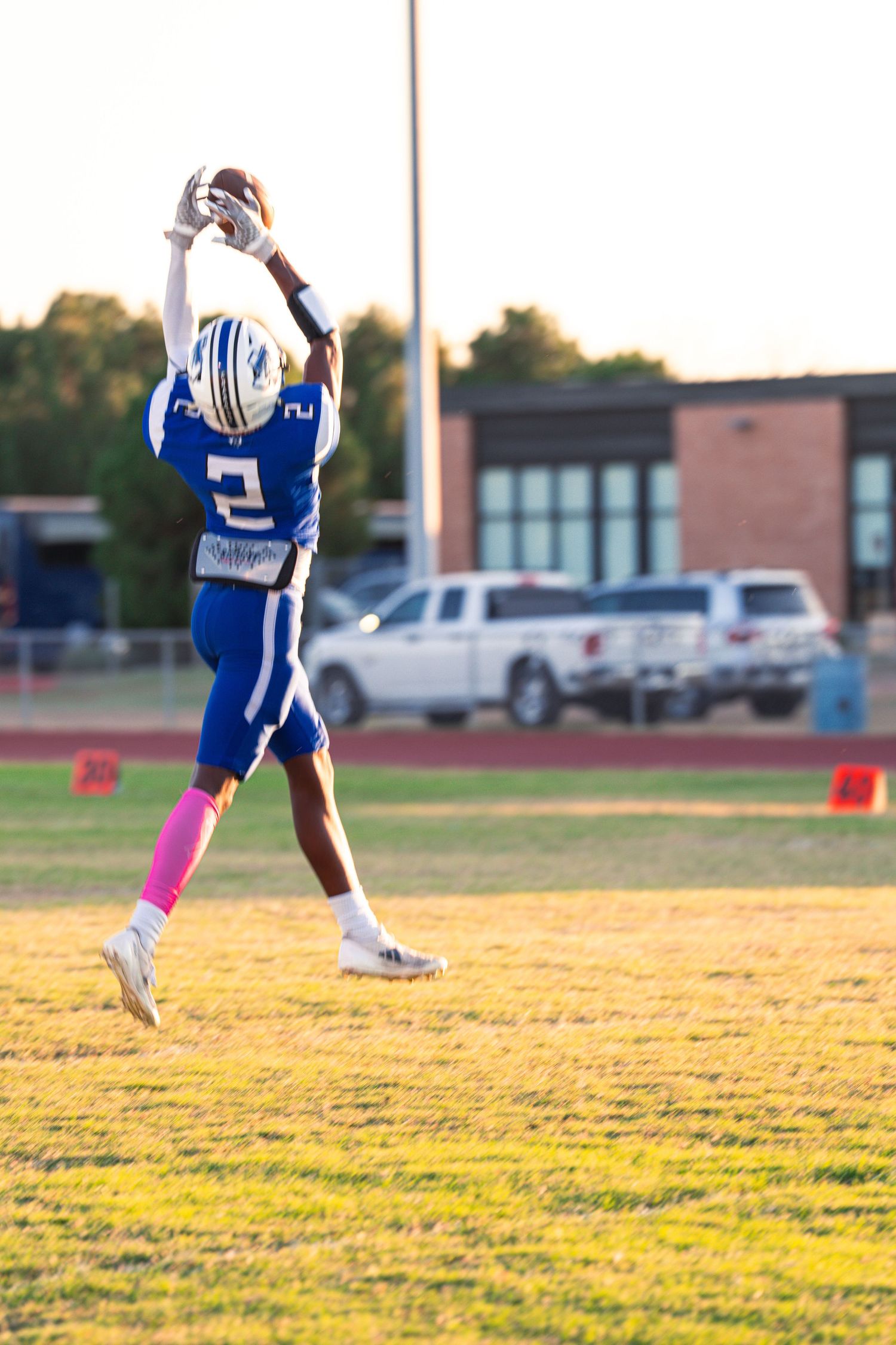 Youth football players in blue and white uniforms run drills on a sunlit practice field.