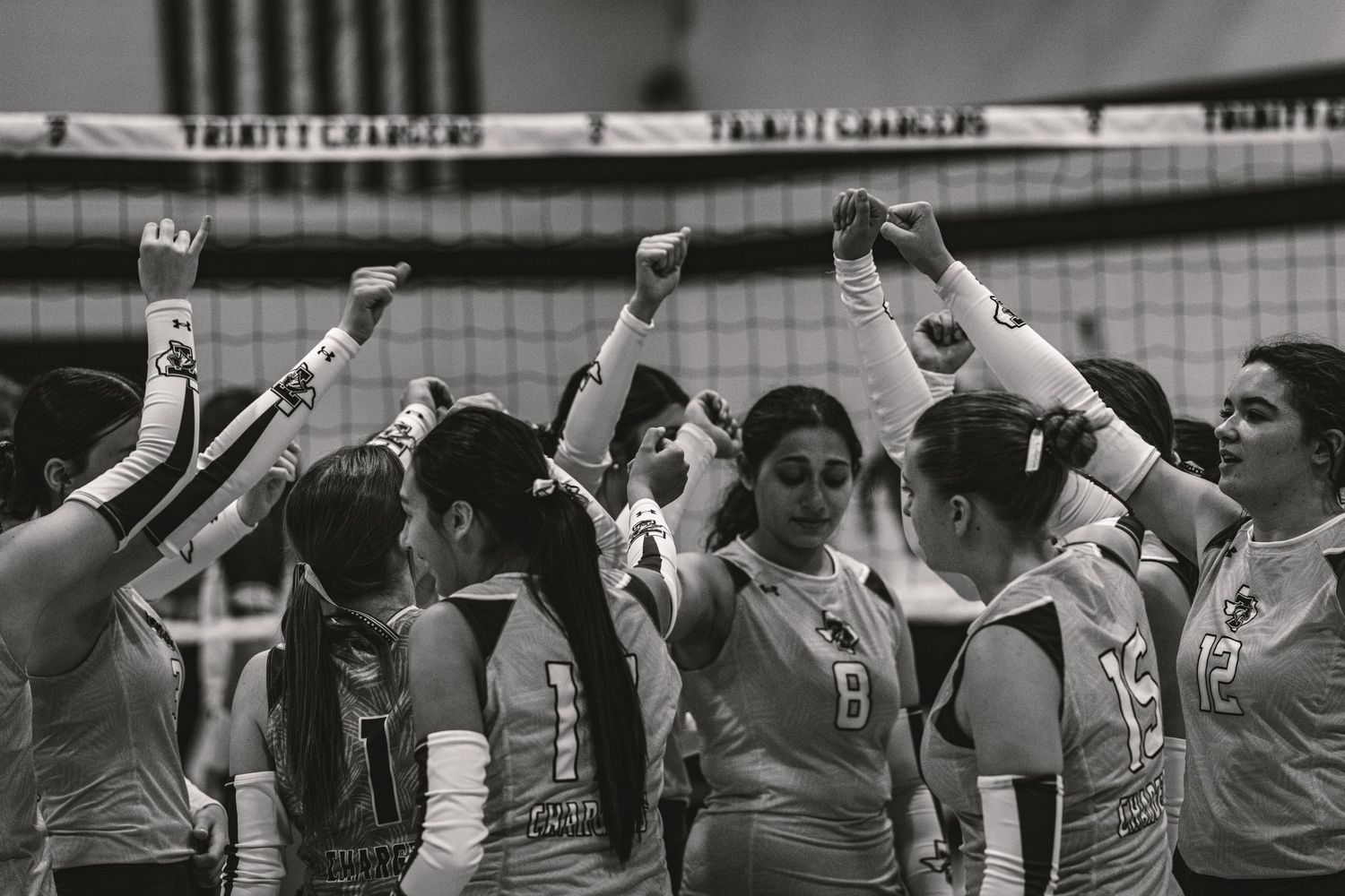 A volleyball team celebrates together with raised fists after scoring during a match in black and white photography.