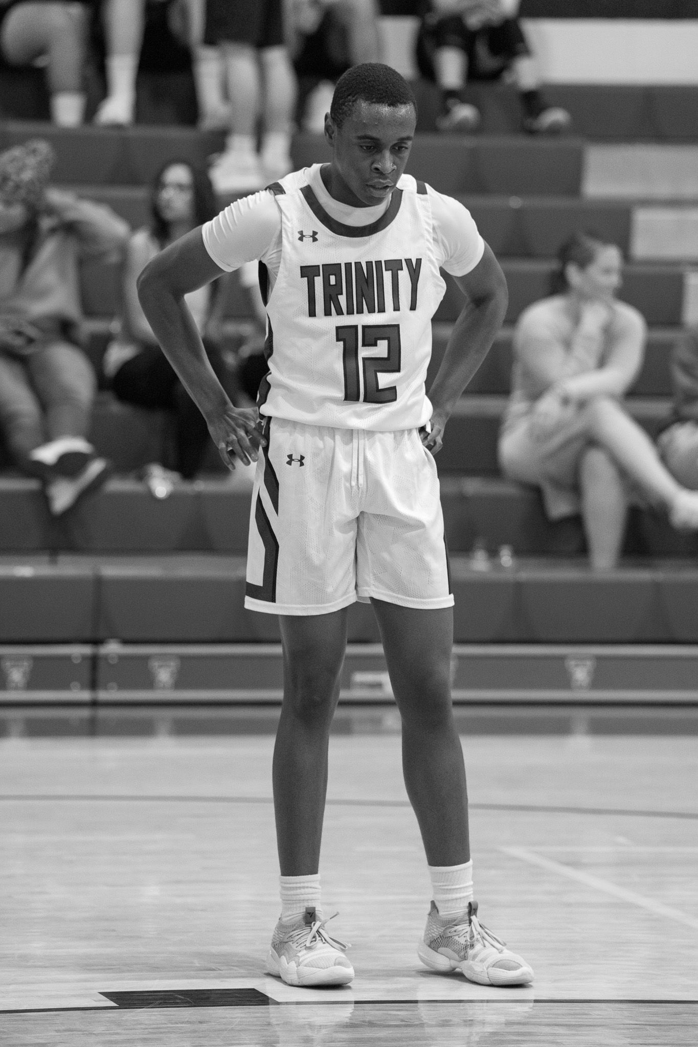 Basketball player in white Trinity jersey bends down on court during game.