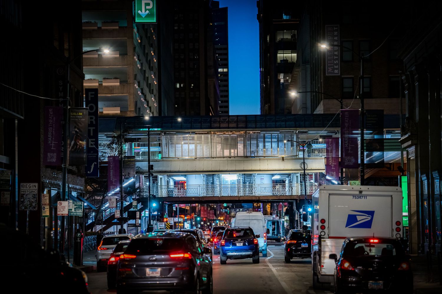 Dark urban cityscape at night with illuminated buildings and parking signs creating a moody atmosphere.