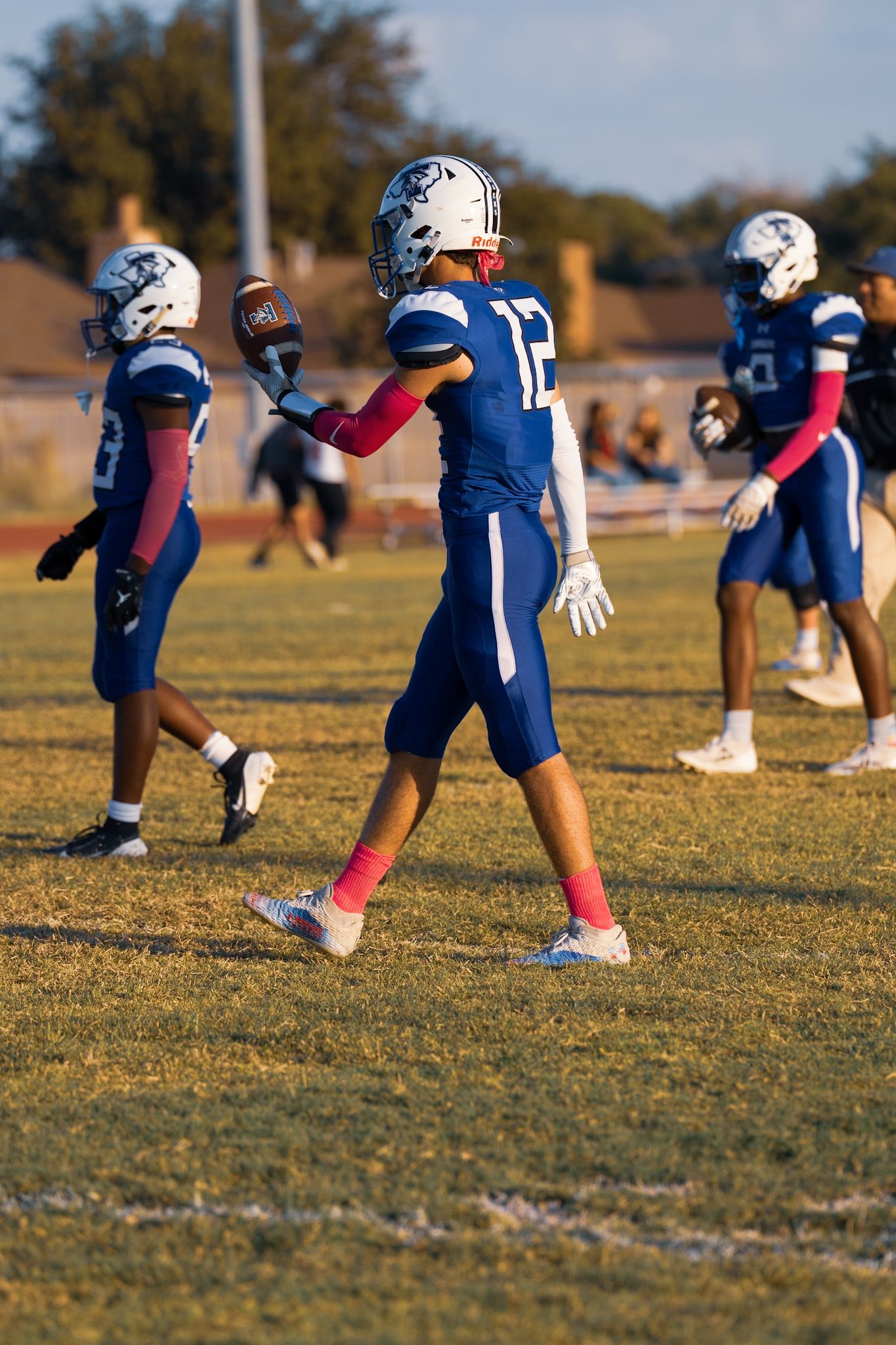 Football players in blue uniforms stretch and warm up on a grassy field during practice.