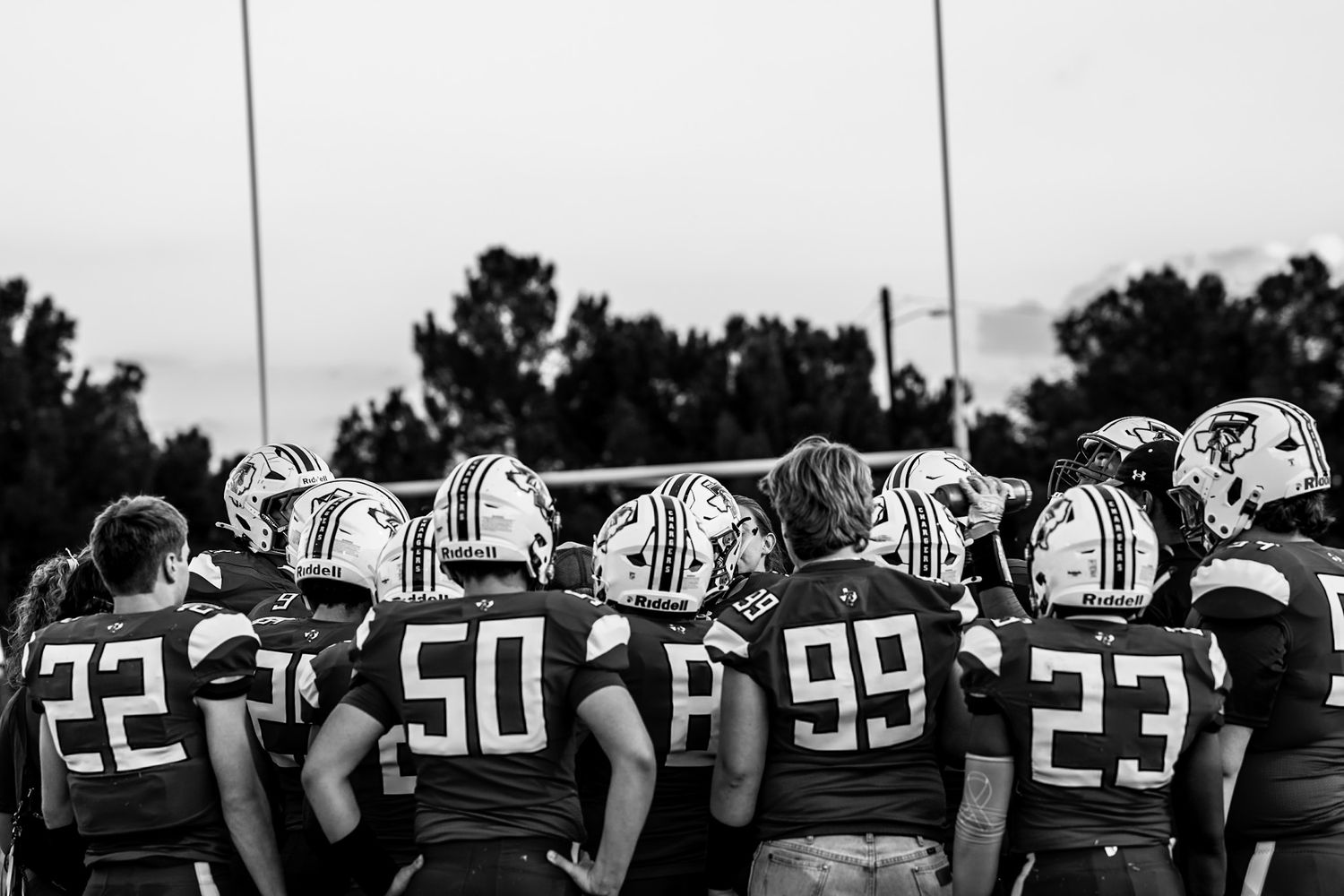 Row of football players in helmets and uniforms standing shoulder to shoulder on field at sunset.