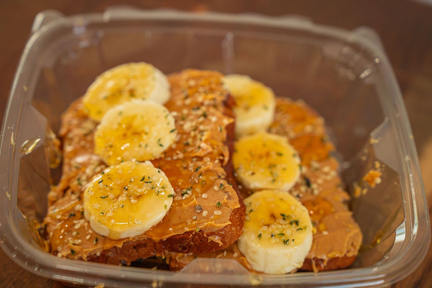 Sliced bananas arranged on top of a caramelized dessert in a clear plastic container.