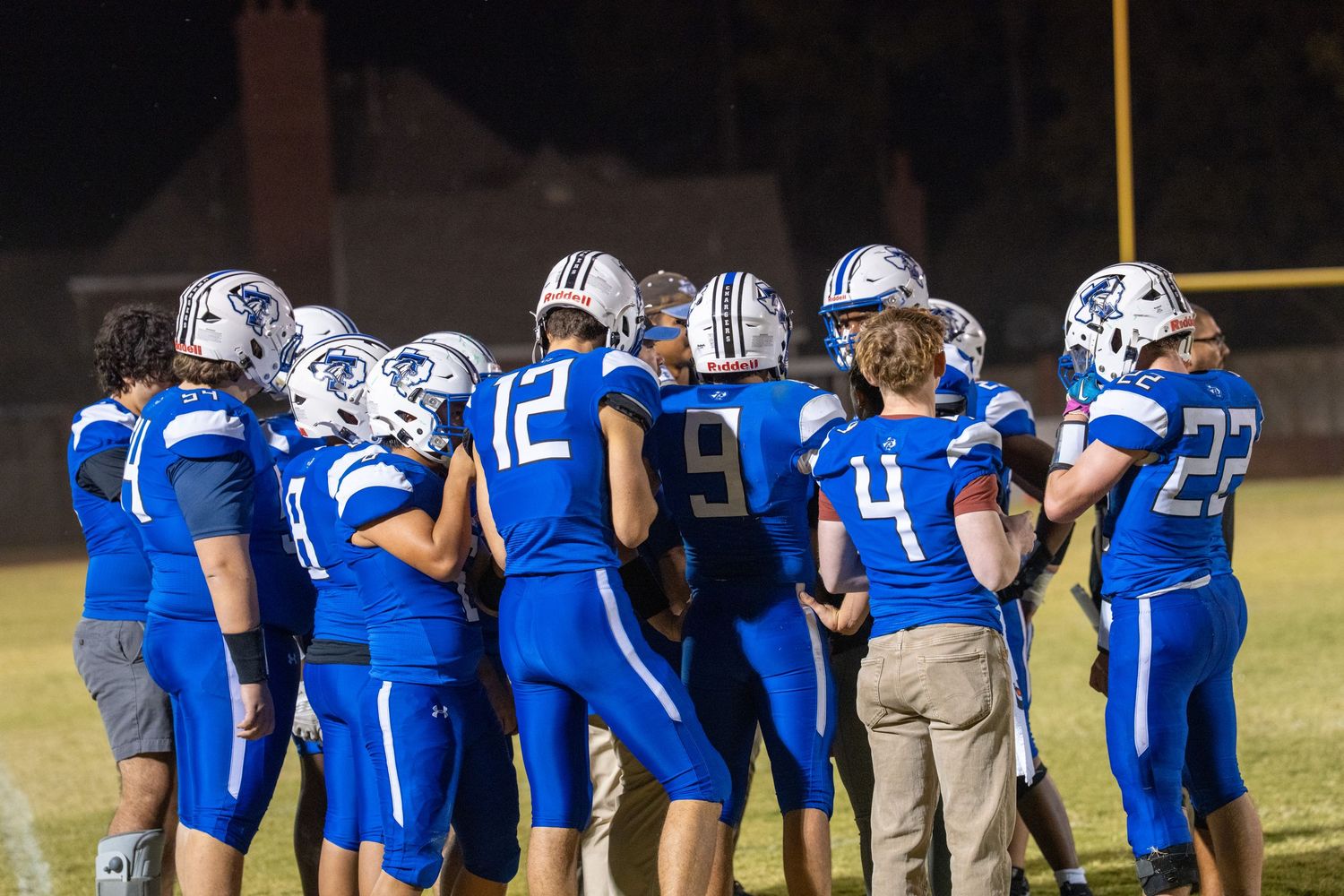 Football players in blue jerseys huddle together on the field during a game.