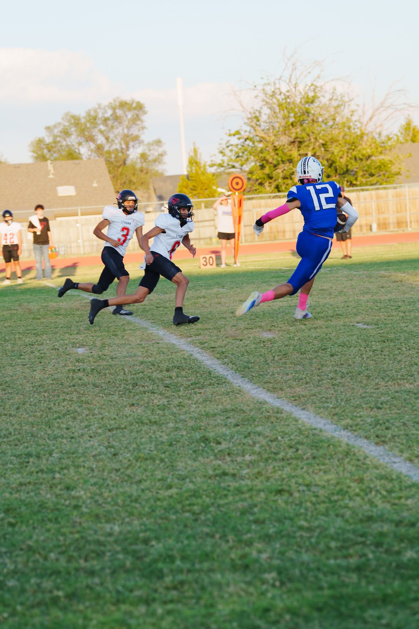 Football players in blue jerseys perform diving drills on a grass field during sunset practice.