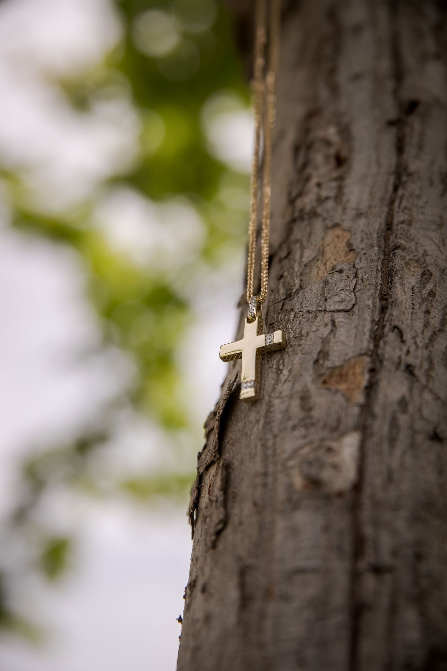 Small decorative cross hanging on a weathered tree trunk with bokeh background.