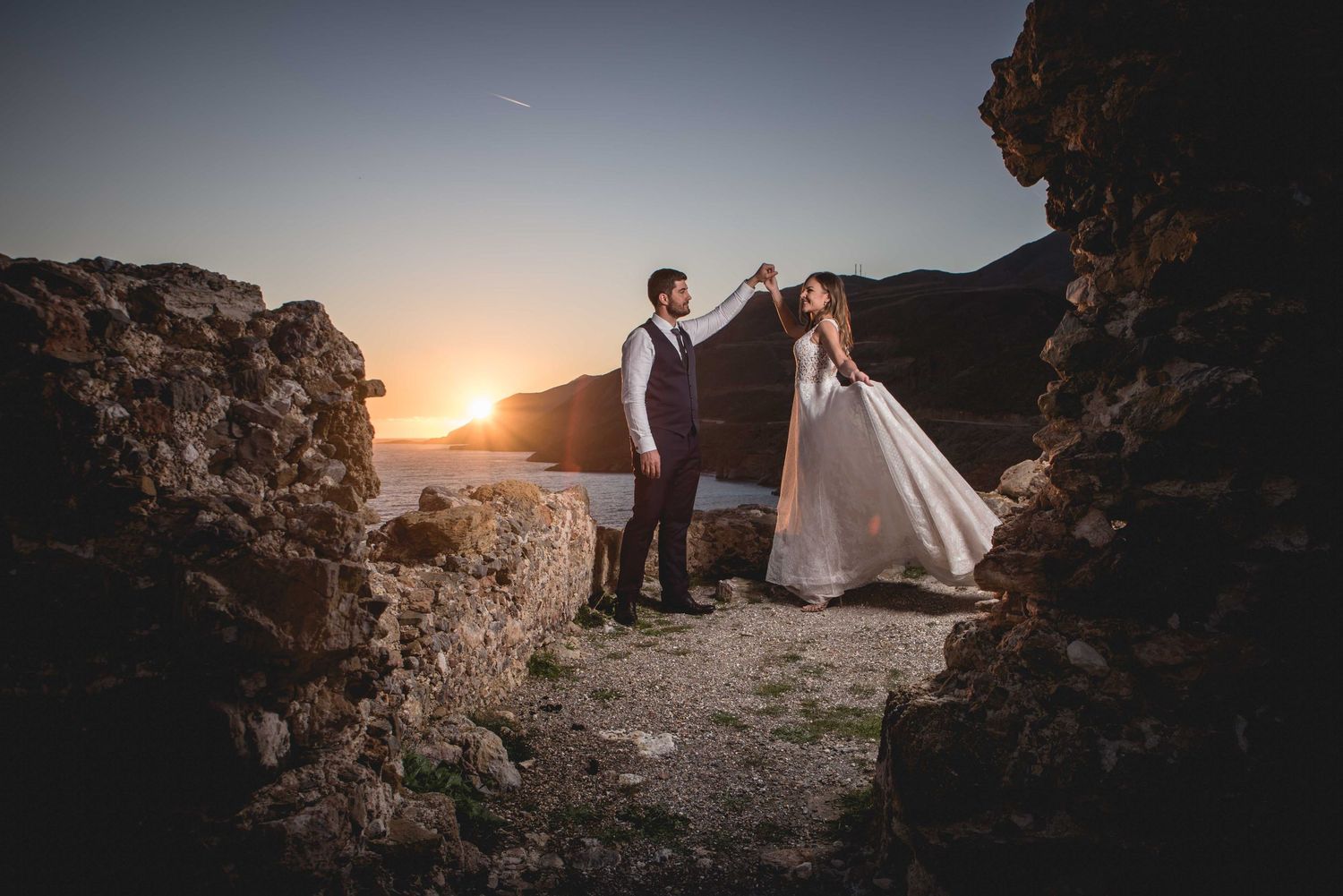 Wedding couple poses on rocky cliff edge during dramatic sunset photo session.